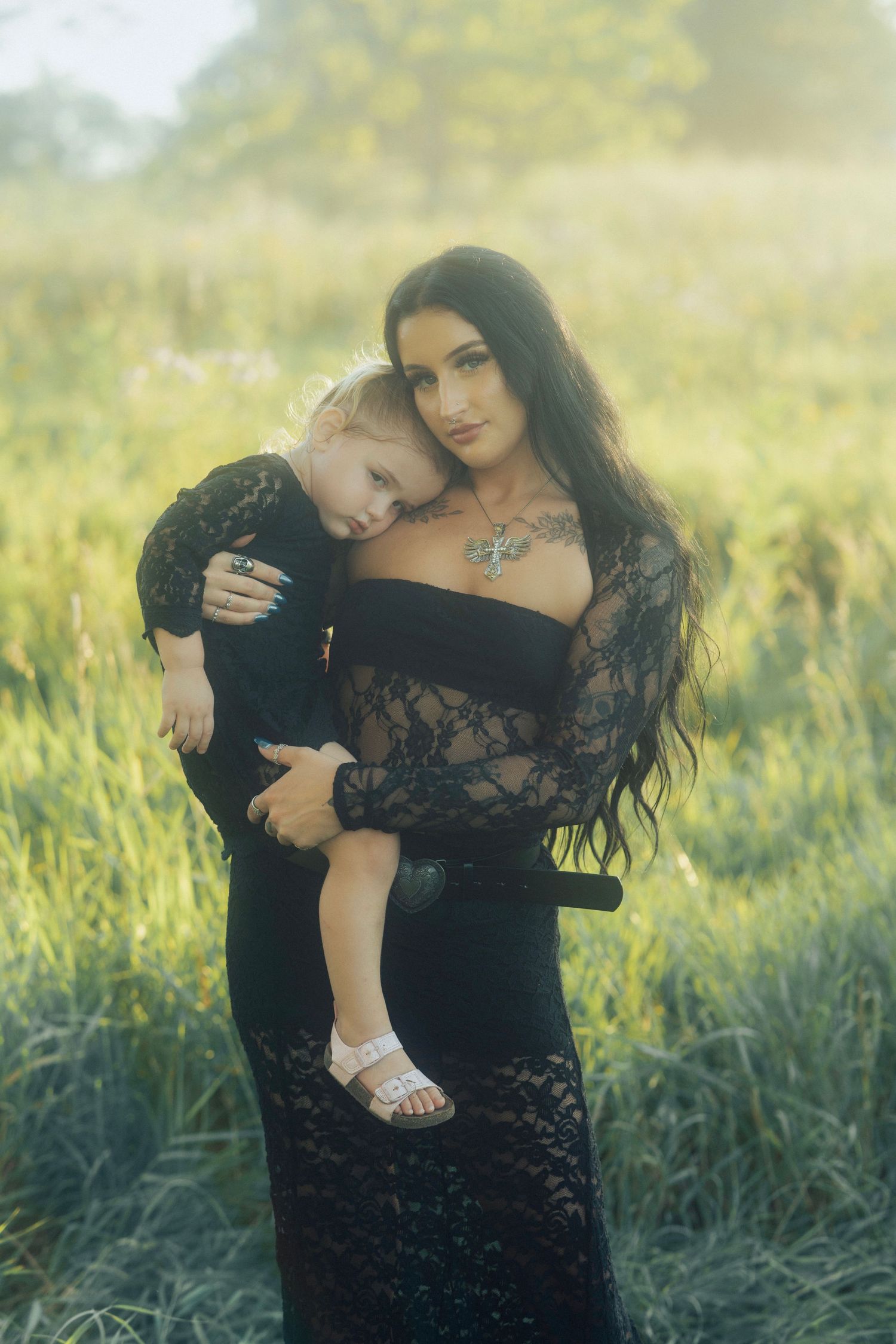 An artistic portrait in a sunlit meadow featuring black lace attire and soft natural lighting.