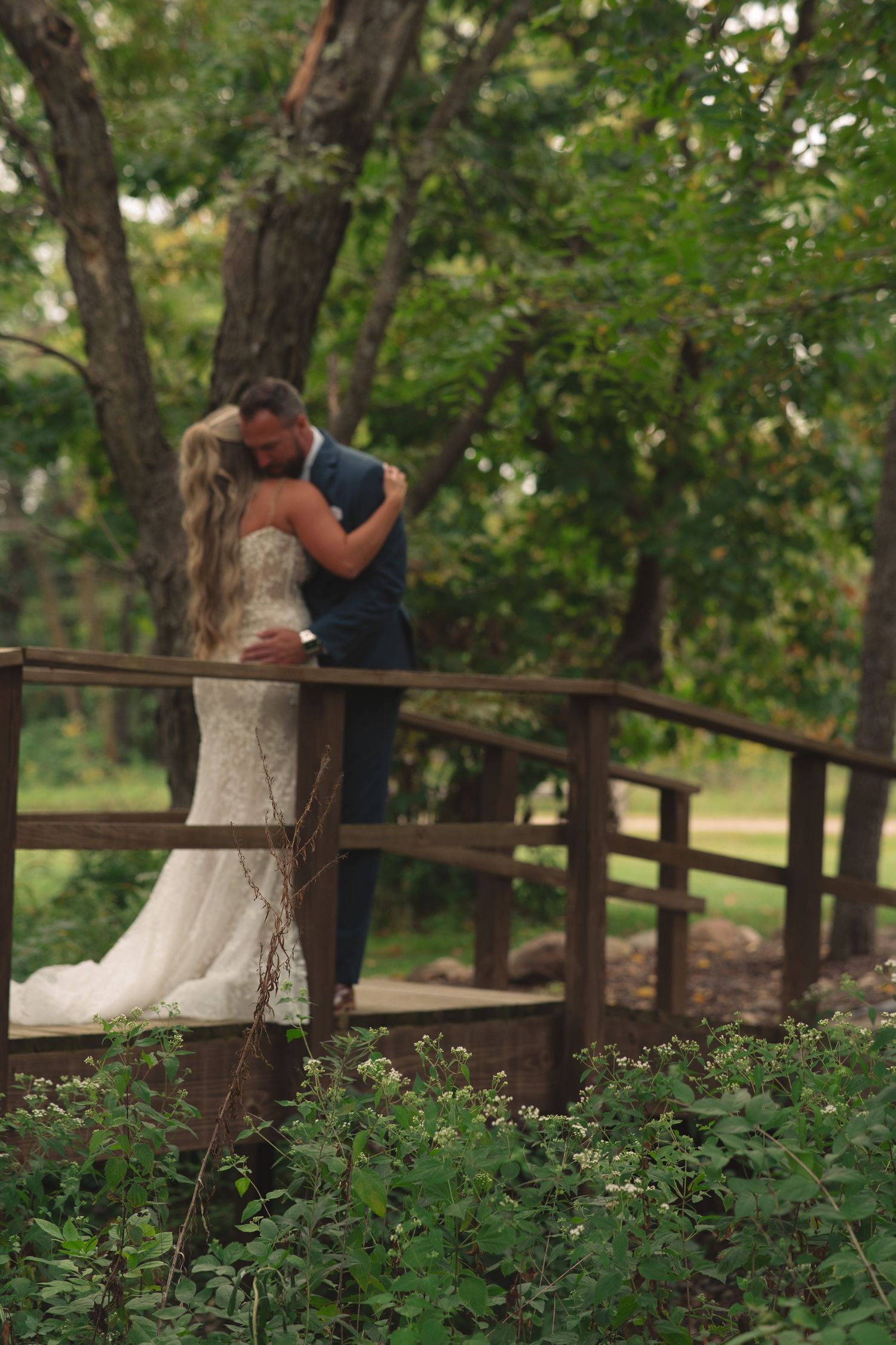 Wedding couple sharing intimate moment on rustic wooden bridge in wooded setting.