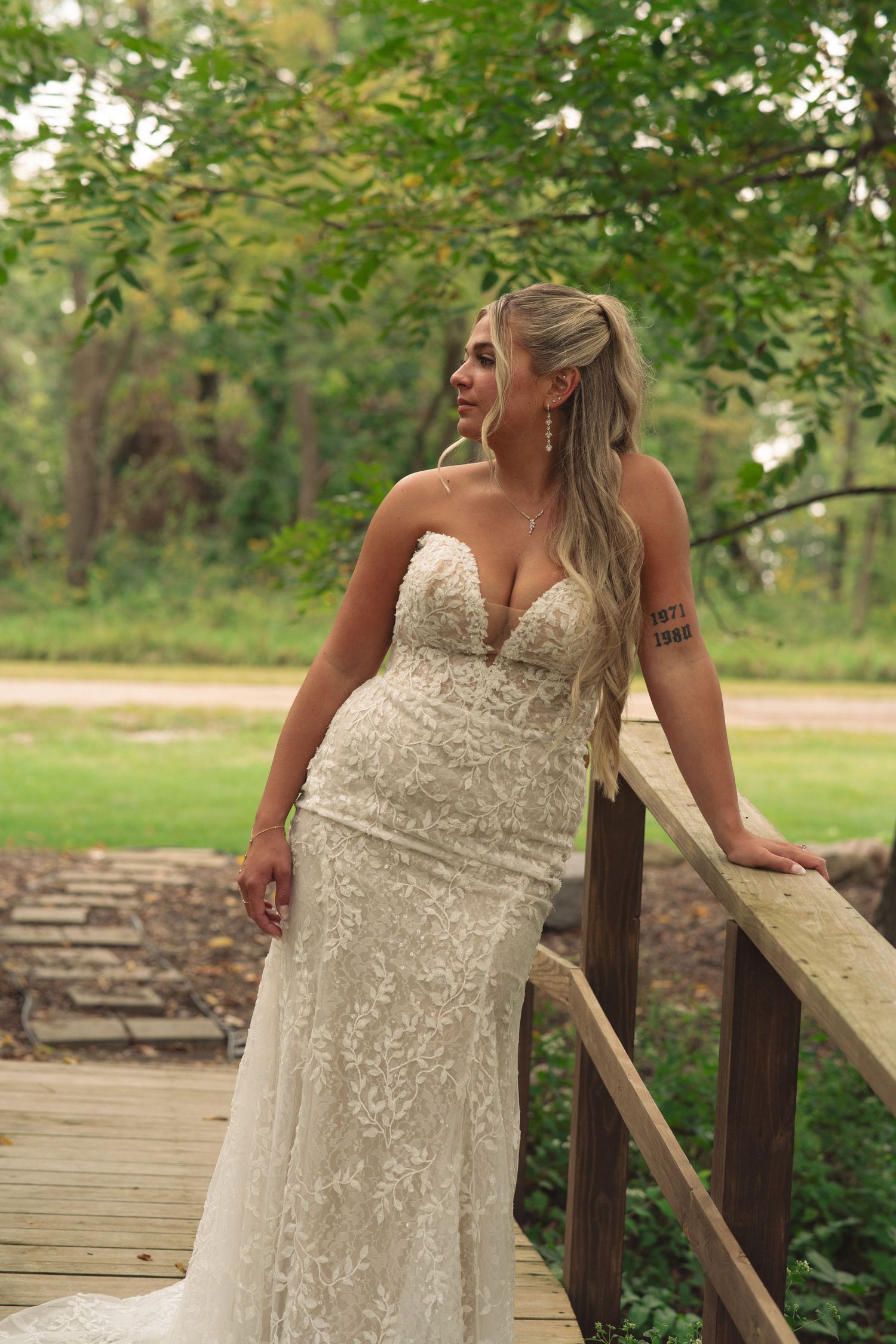 Bride in sequined wedding gown posing on wooden deck surrounded by greenery.