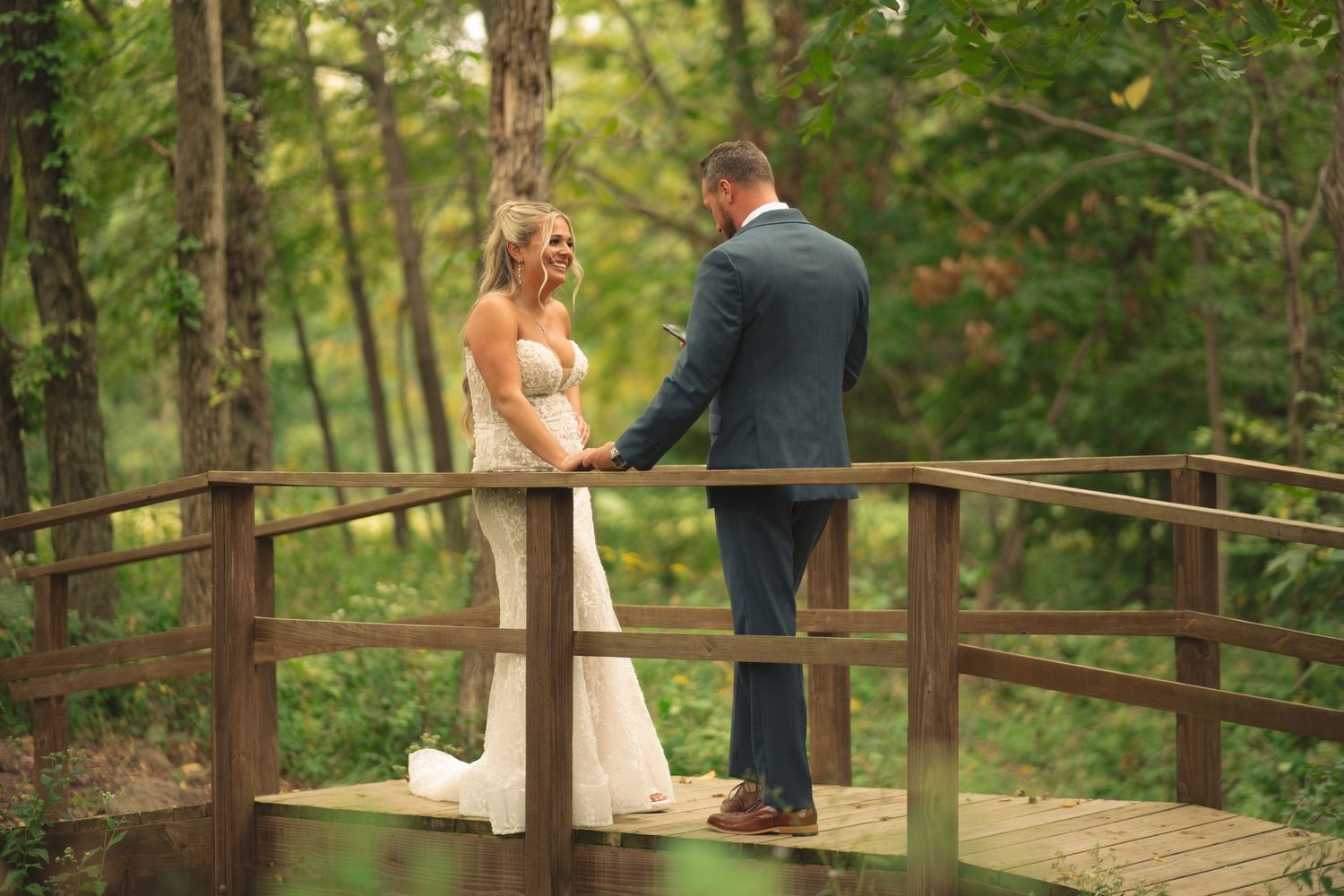 Romantic wedding photos on a wooden bridge surrounded by lush green forest.
