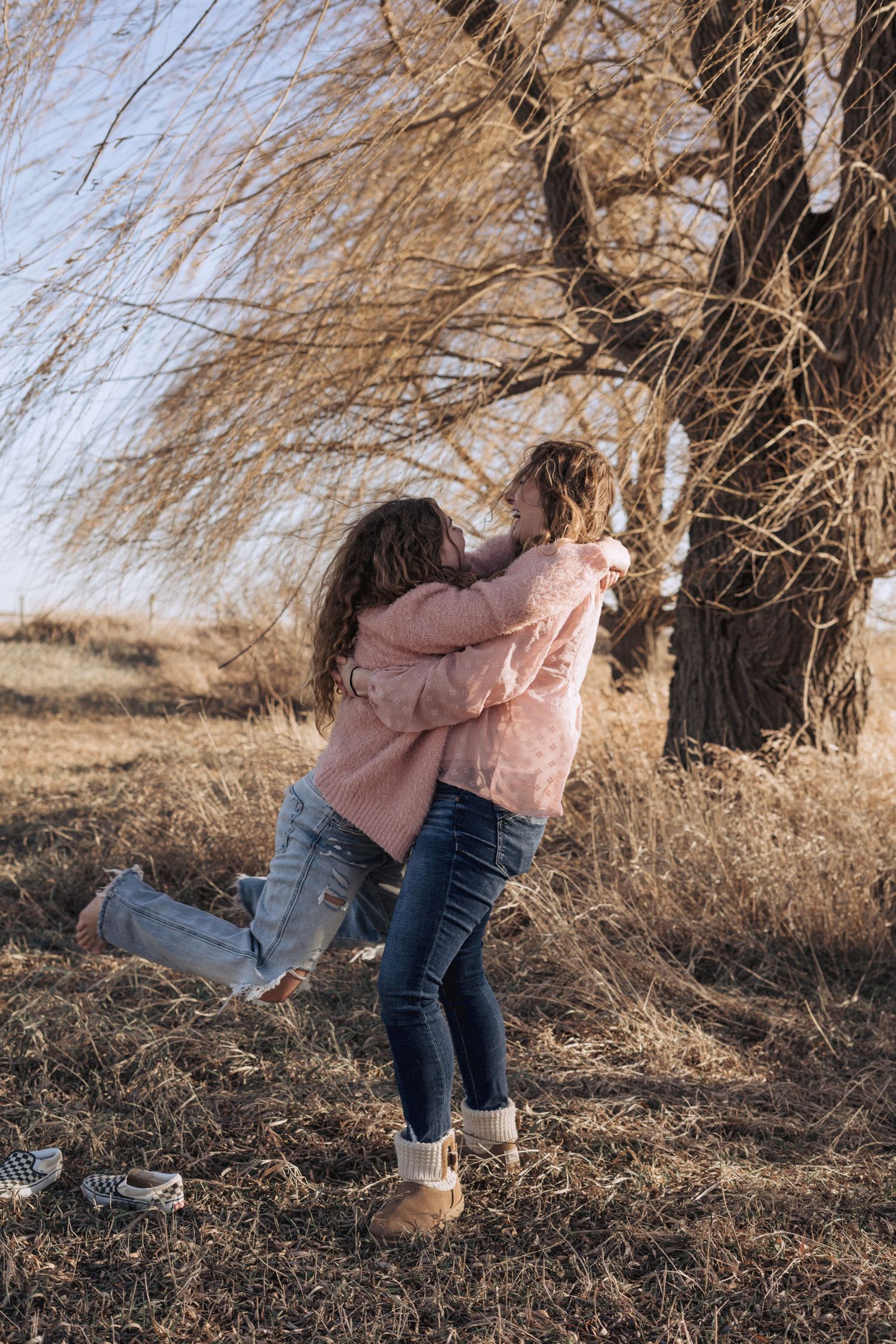 Person in pink jacket and jeans poses playfully among bare winter trees.