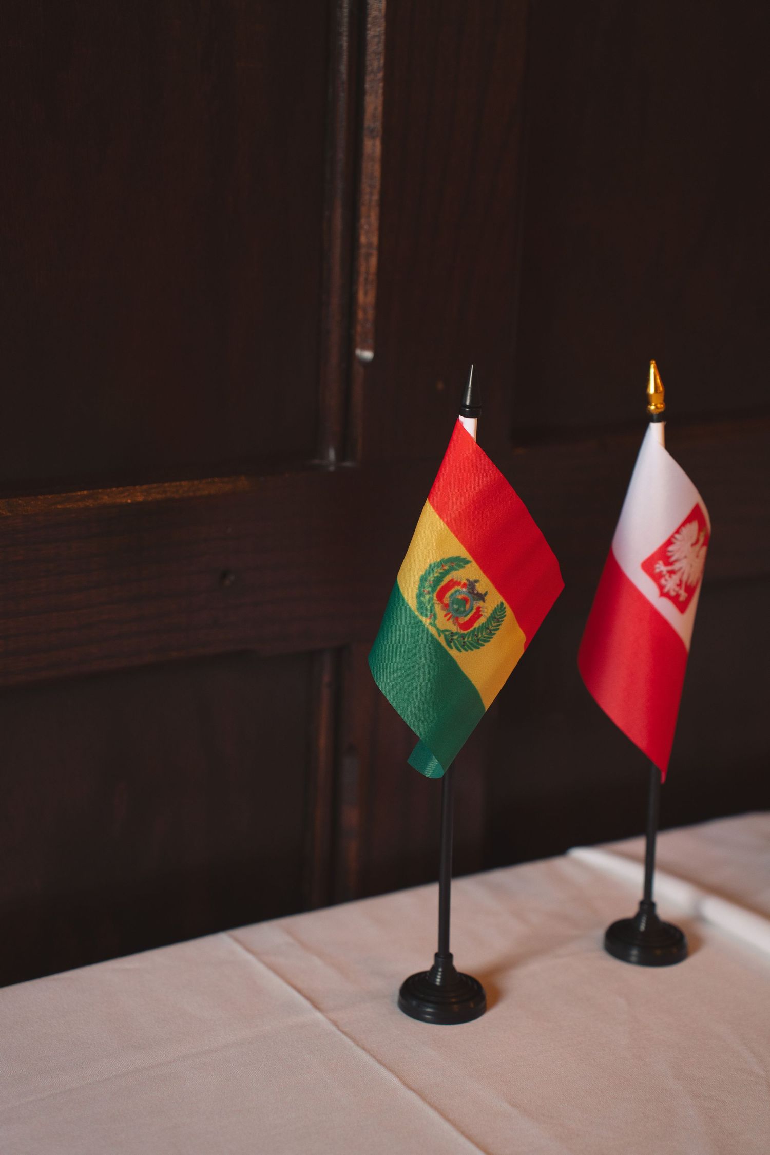 Small national flags of Bolivia and Peru displayed on stands against a dark wooden backdrop.
