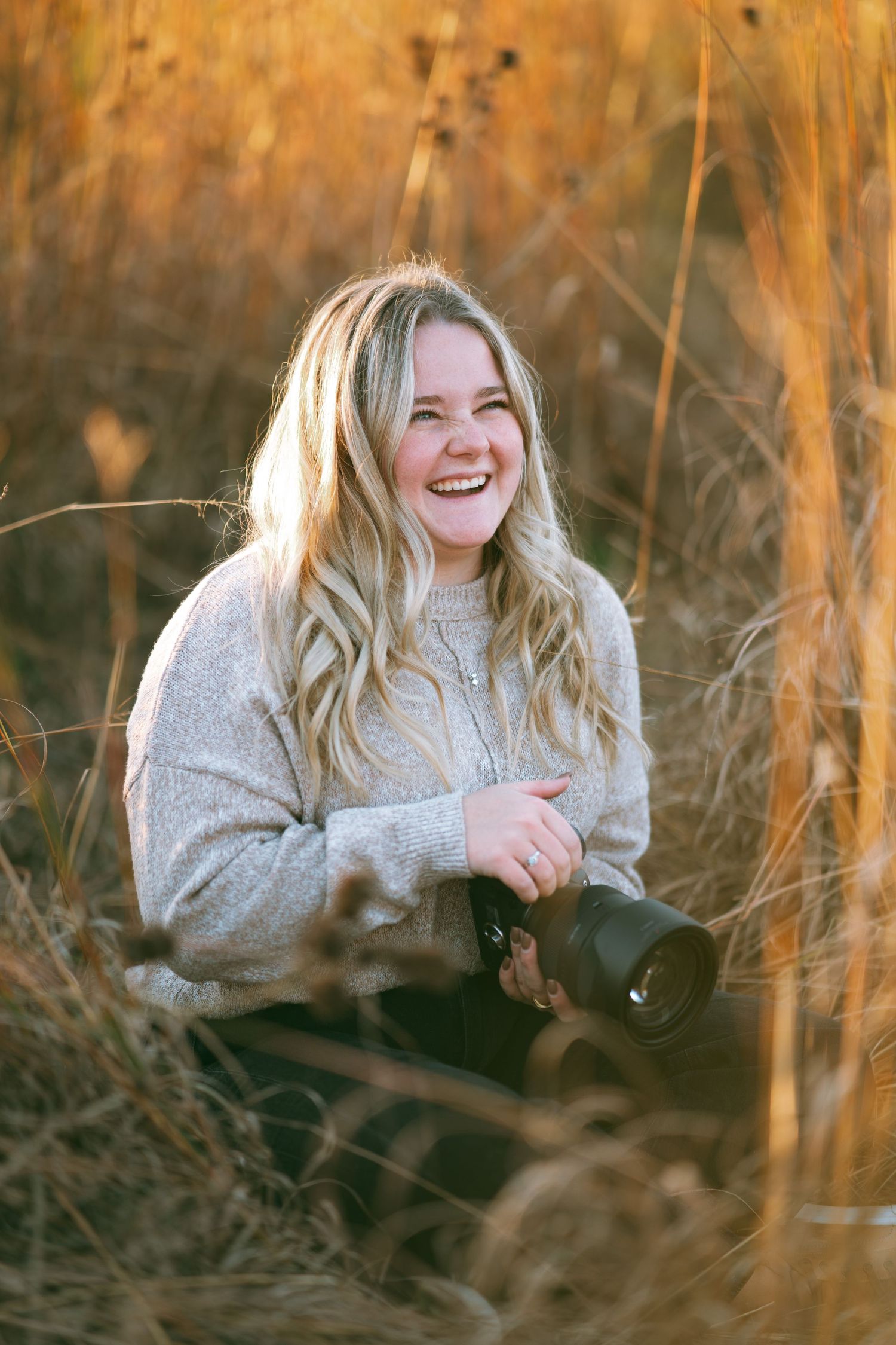 Person in cream sweater lying in golden tall grass during sunset.