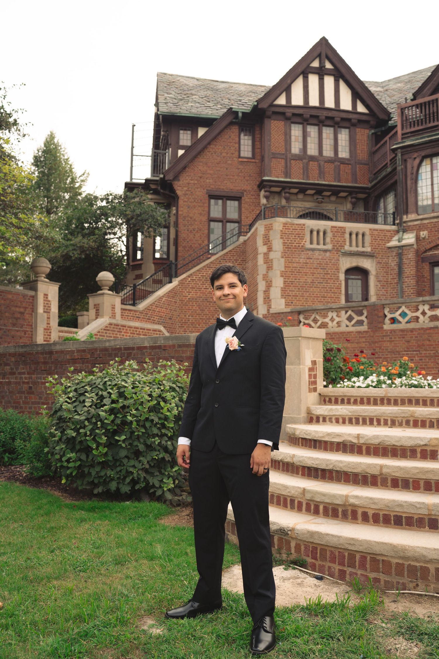 Wedding couple poses separately on elegant brick steps of Tudor mansion.