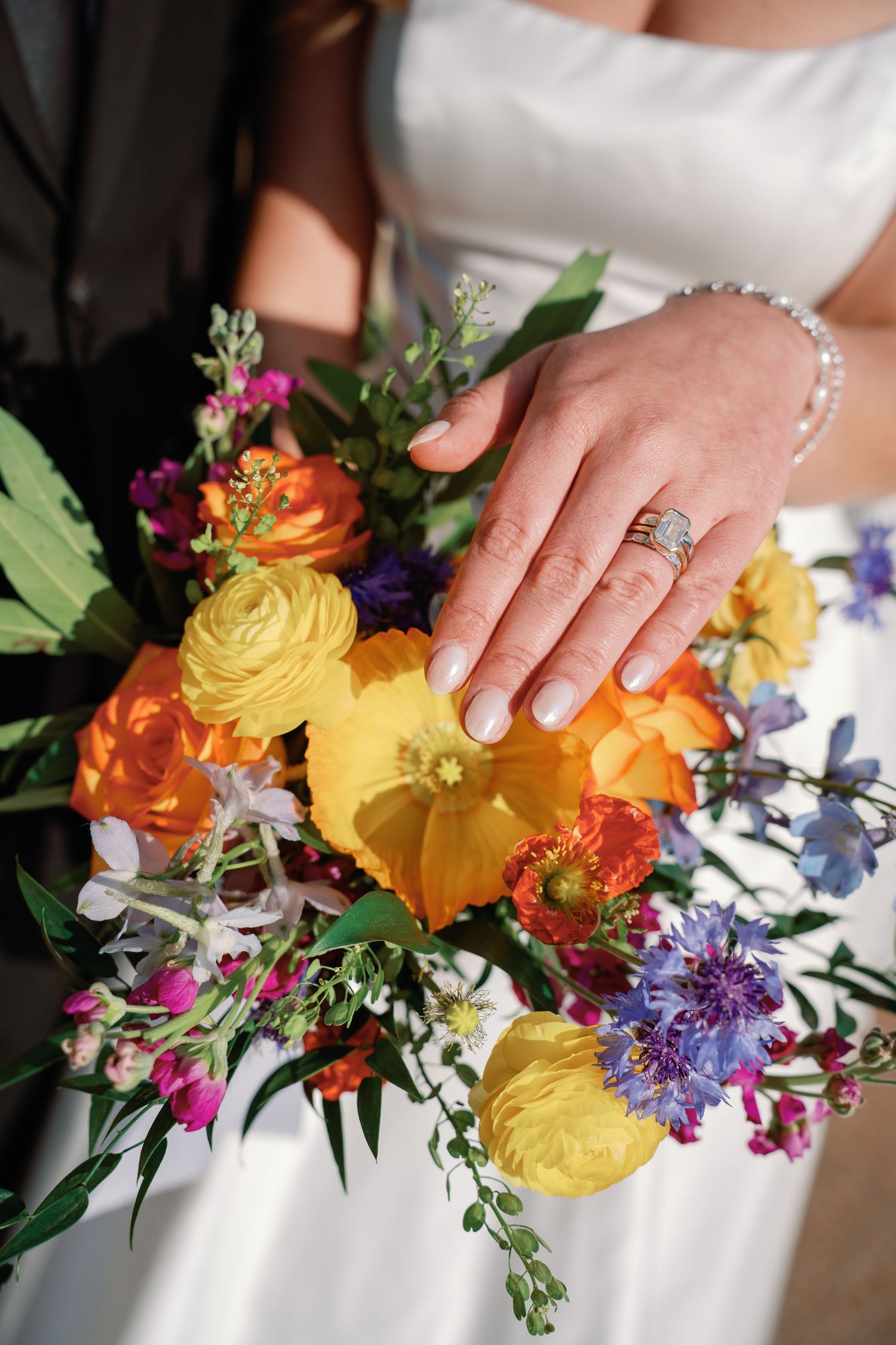 Bride displays wedding ring on colorful bouquet with orange, yellow, and purple flowers at wedding ceremony.
