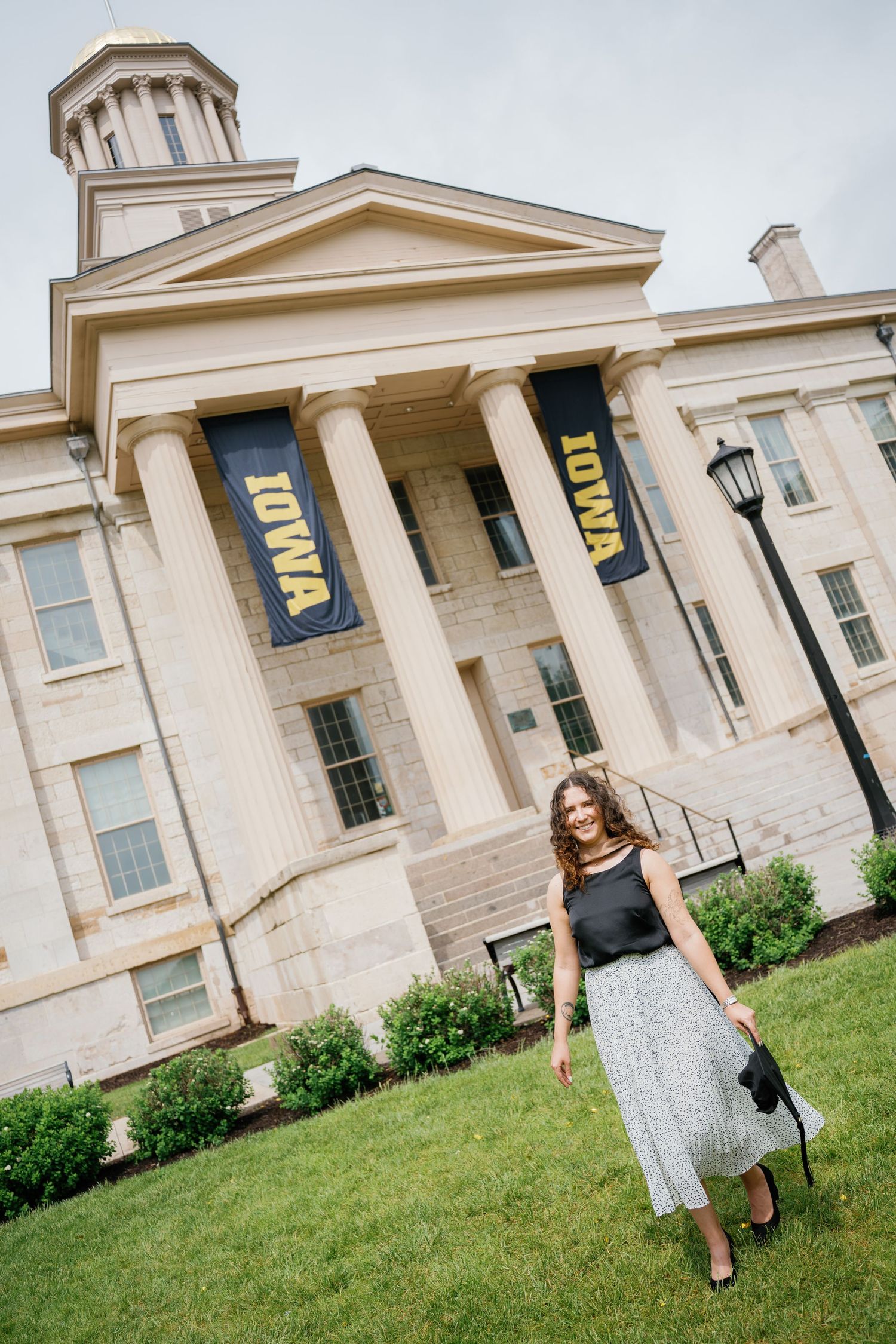 A woman stands in front of the University of Iowa Old Capitol building adorned with black and gold IOWA banners.