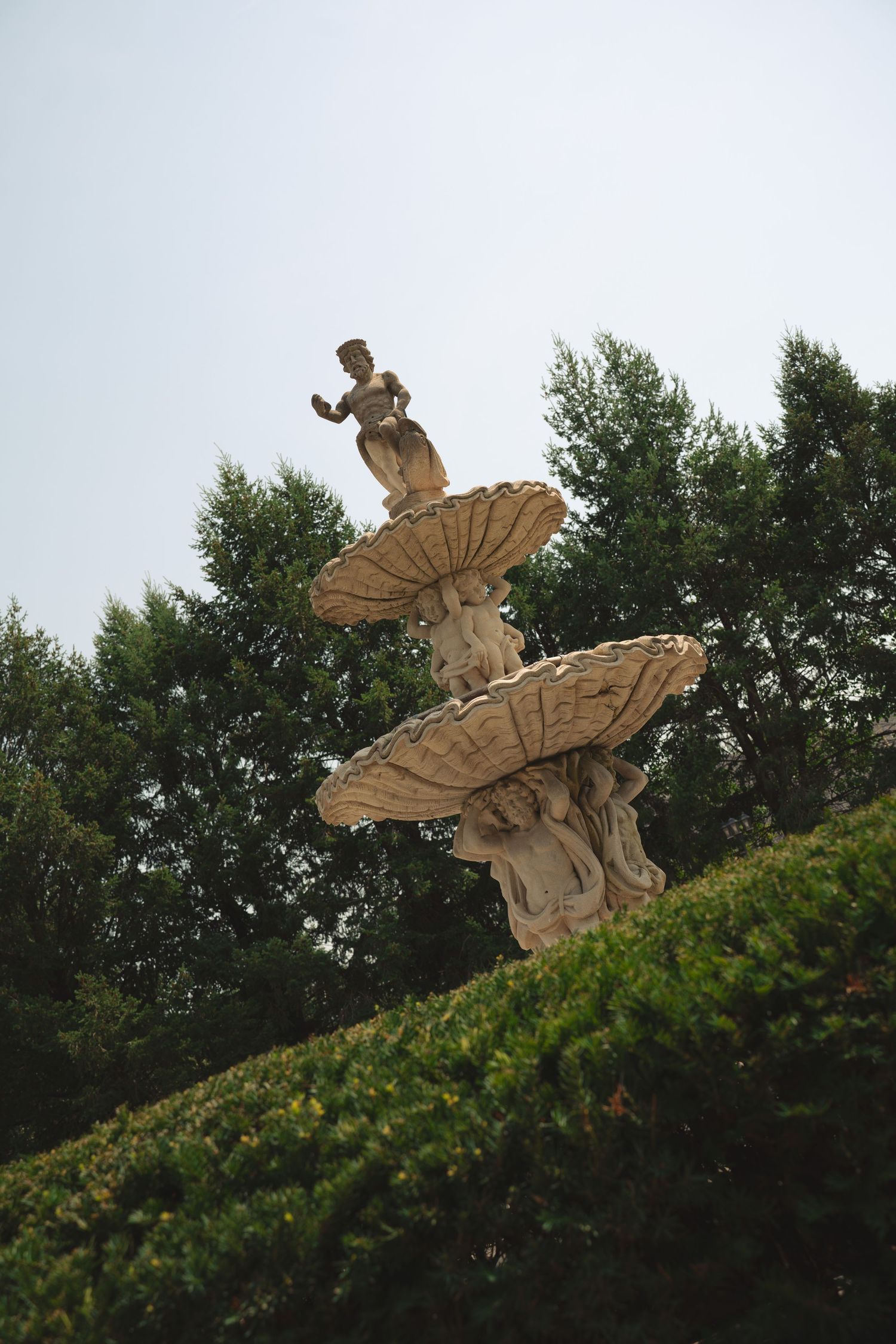 Stone angel statues perched atop a garden wall against an overcast sky.