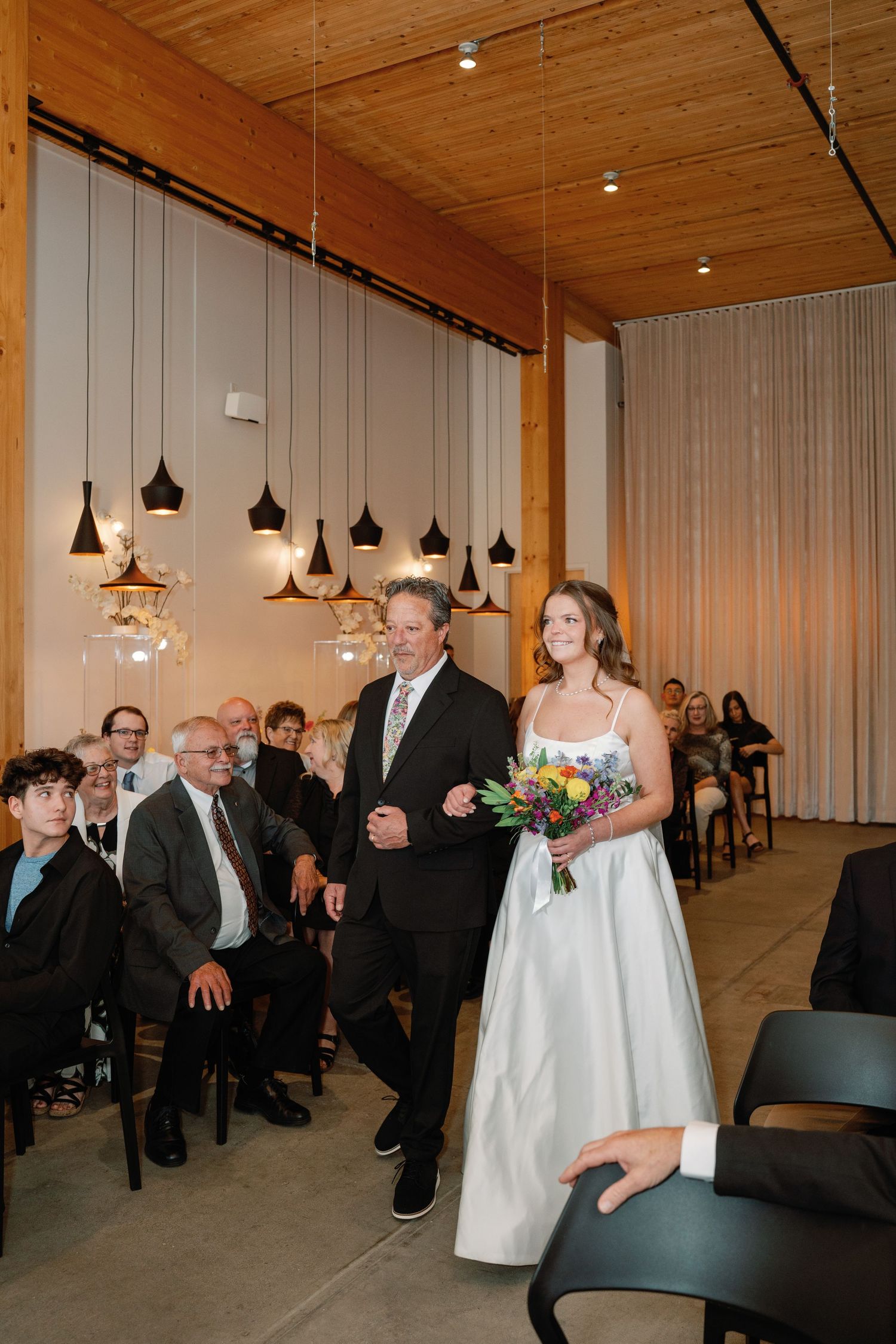 Bride in white gown walks down the aisle with her father at an elegant indoor wedding ceremony.