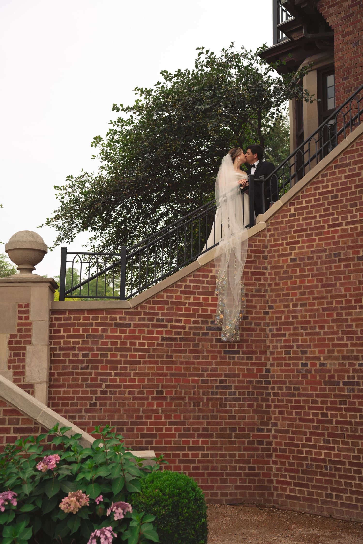 Couple shares intimate moment on brick terrace with flowering garden below.