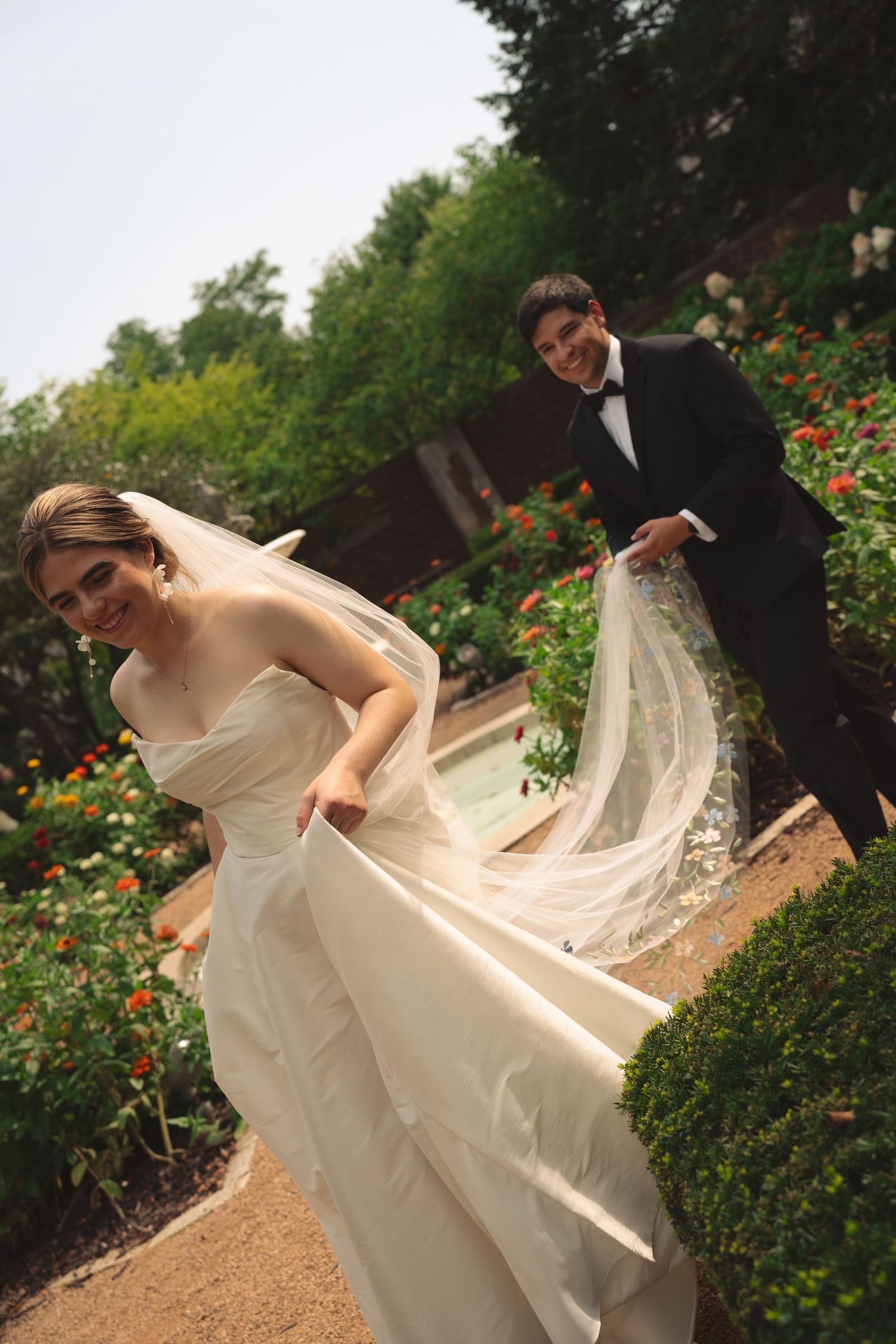 Bride's white dress and veil flow elegantly during outdoor wedding photoshoot.