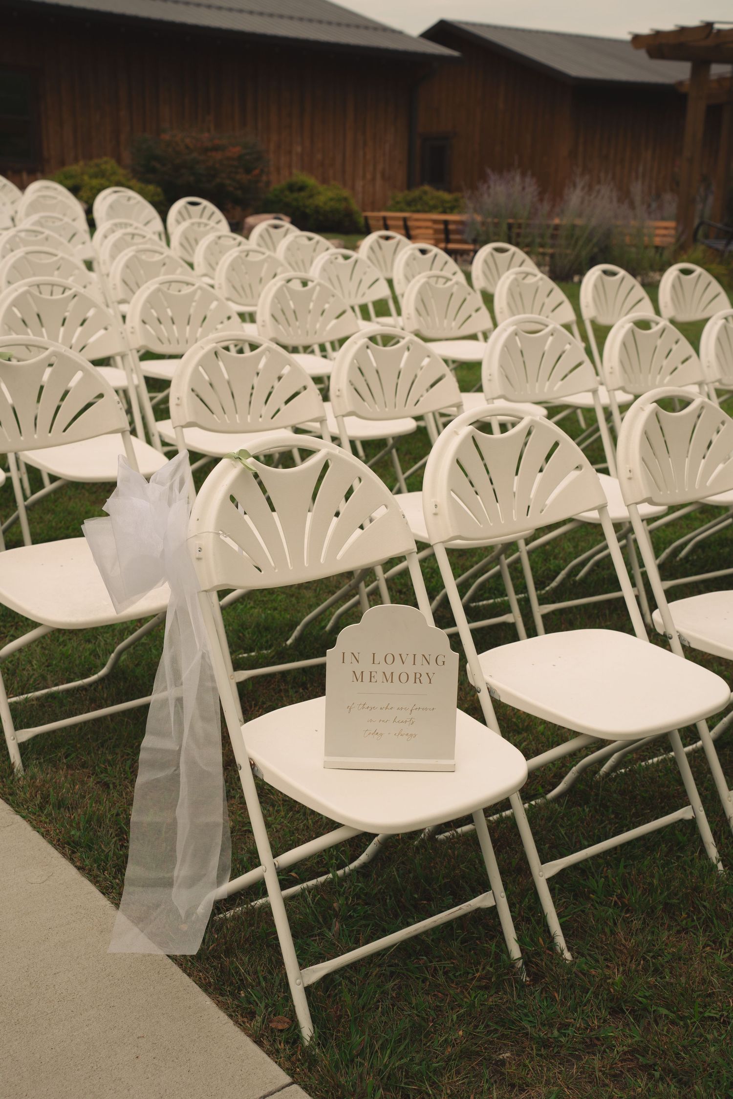 White folding chairs with sheer fabric decorations arranged for outdoor wedding ceremony.