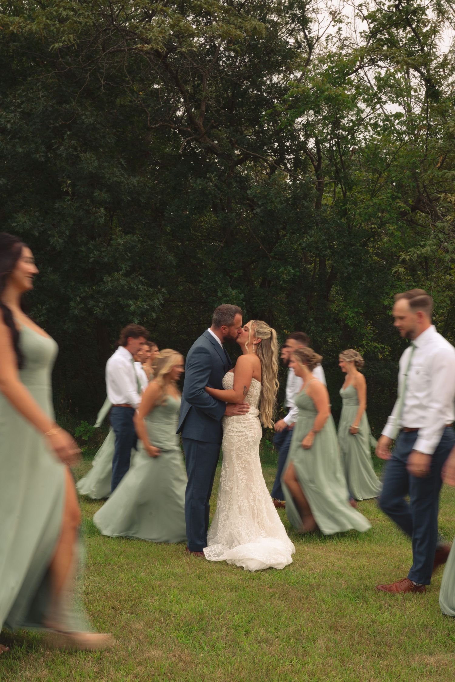 Wedding group performs choreographed falling sequence on grass during photo session.