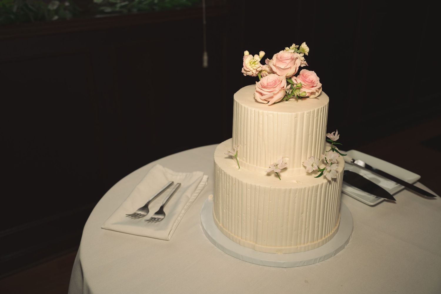 Elegant white wedding cake with delicate floral decorations against dark background.