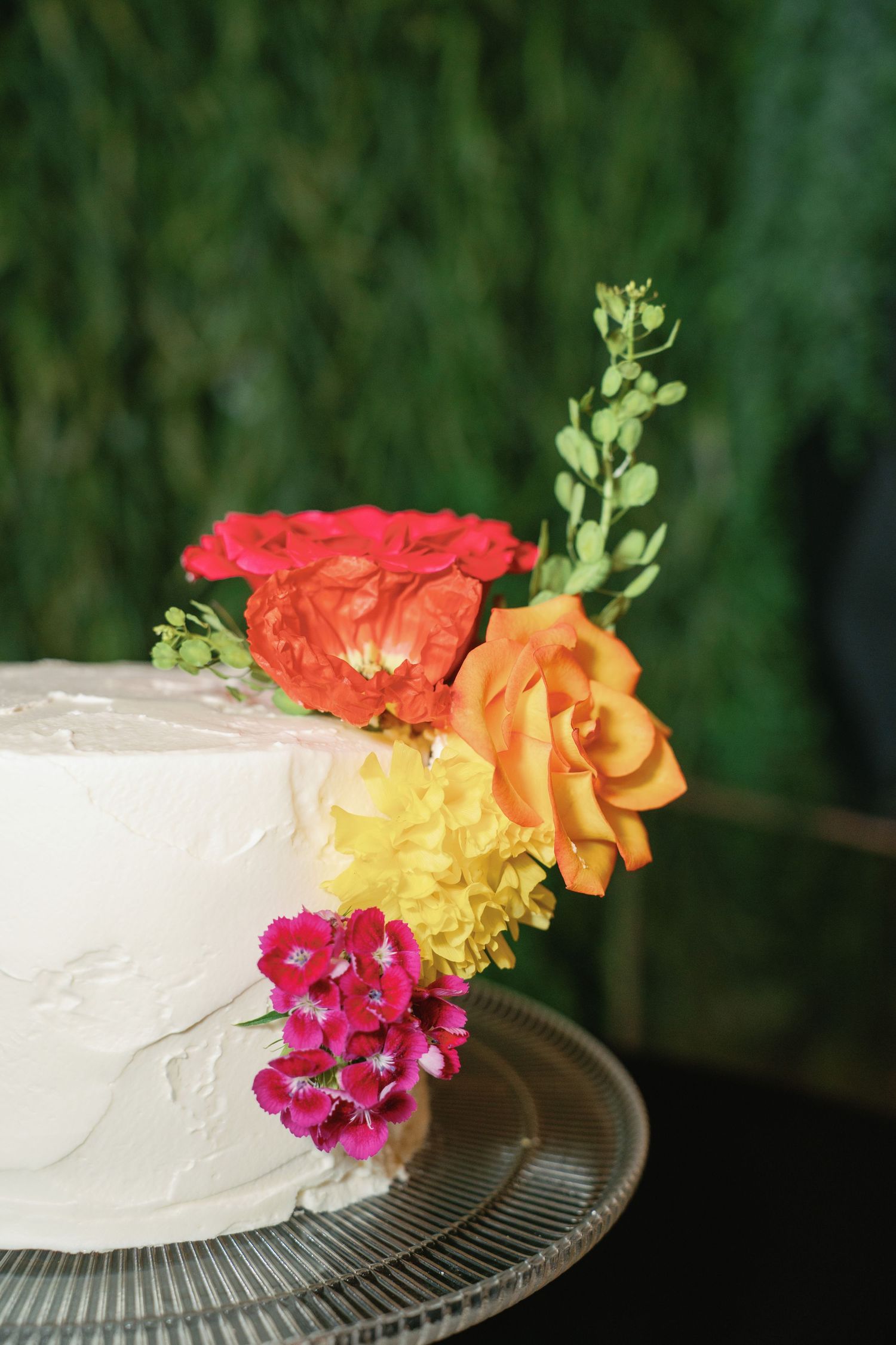 Elegant white wedding cake topped with colorful red, orange, yellow, and pink flowers.