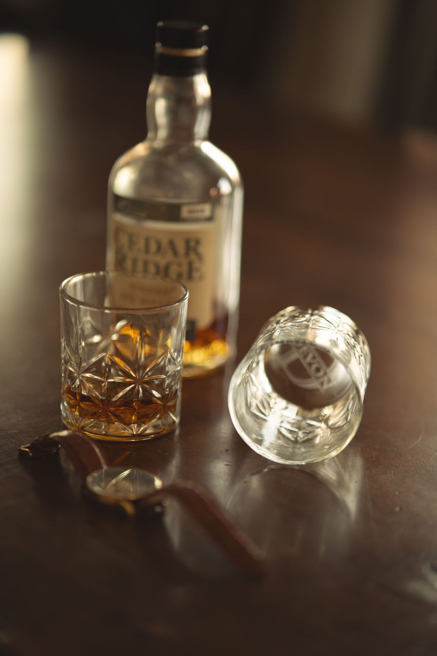 Artistically lit whiskey glasses and Cedar Ridge bourbon bottle arranged on dark wood.