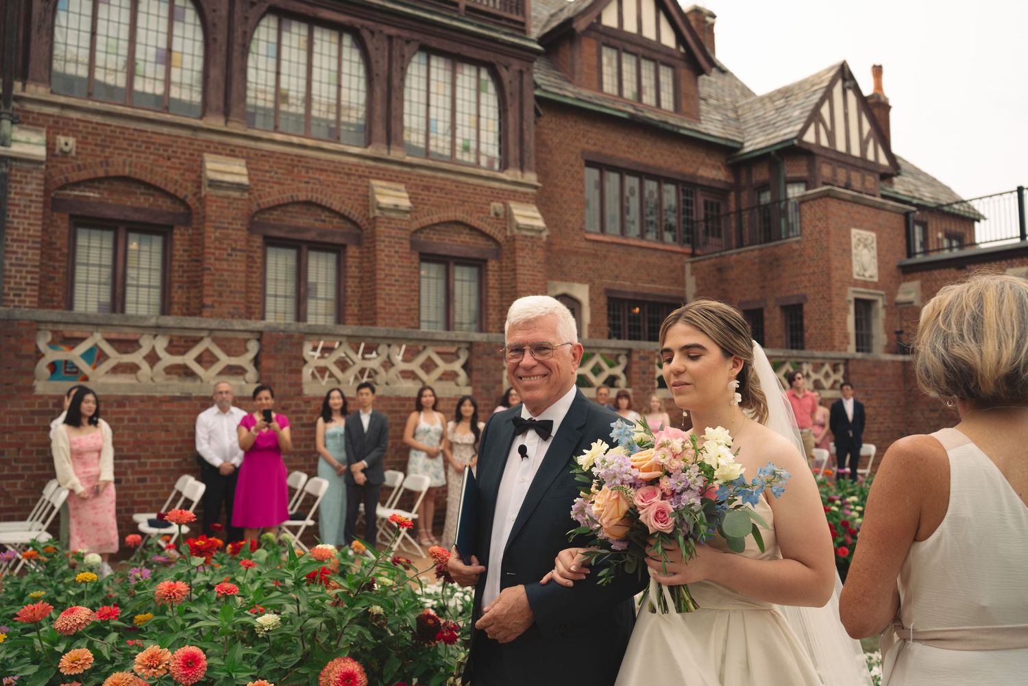 Wedding ceremony setup with floral arrangements outside Tudor-style brick building.