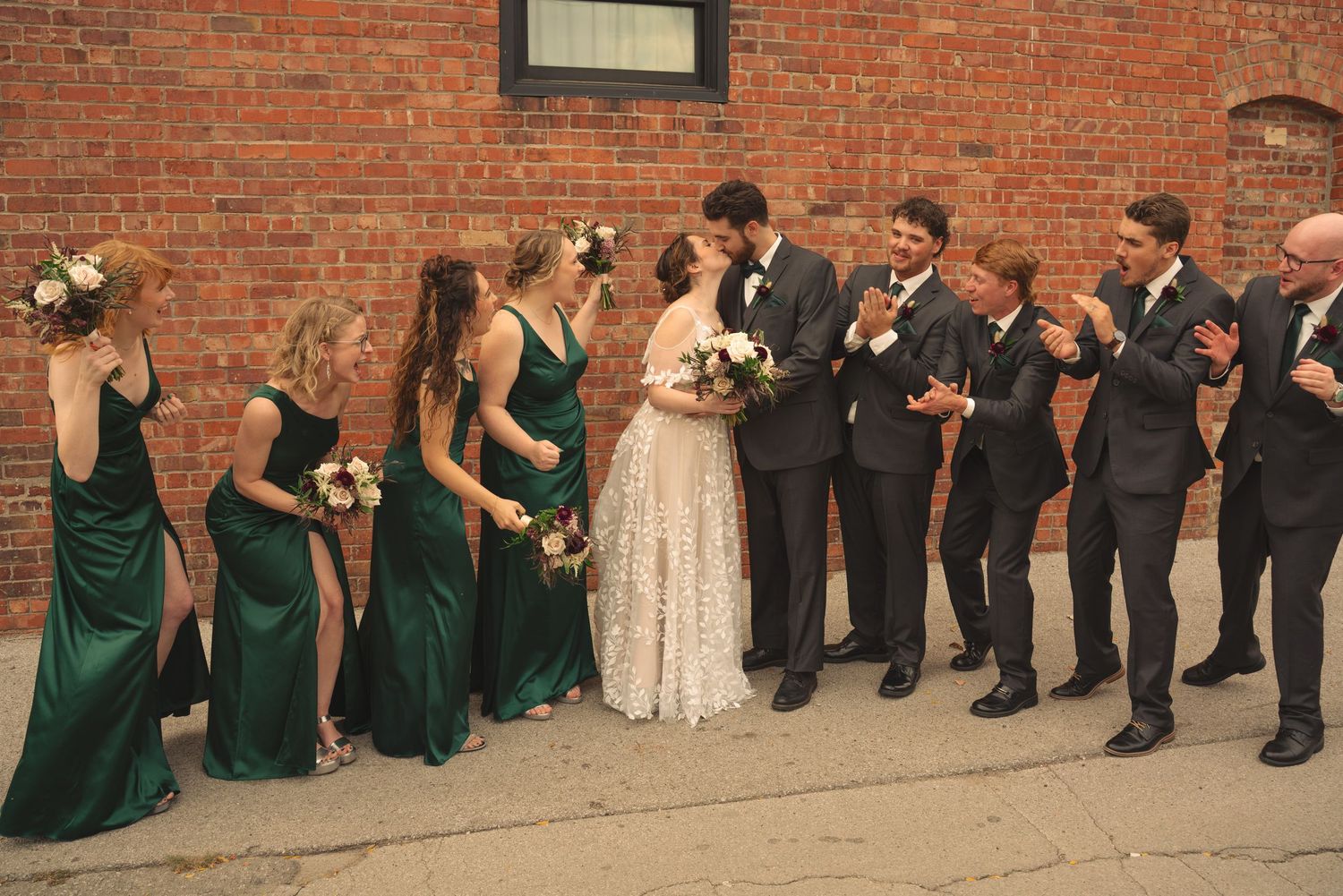 Wedding party lined up against brick wall in coordinated formal attire.