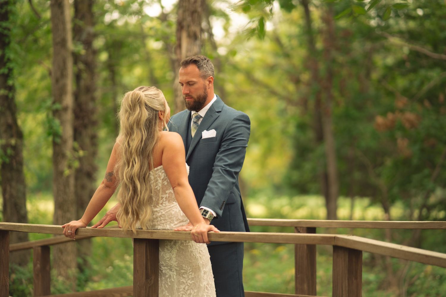 Romantic wedding portraits taken on wooden bridge pathway through green forest.