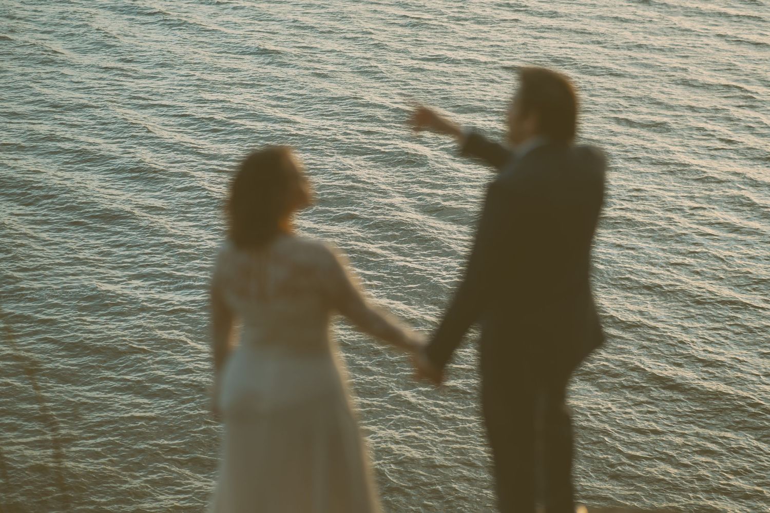 Silhouettes of people walking along waterfront at sunset.