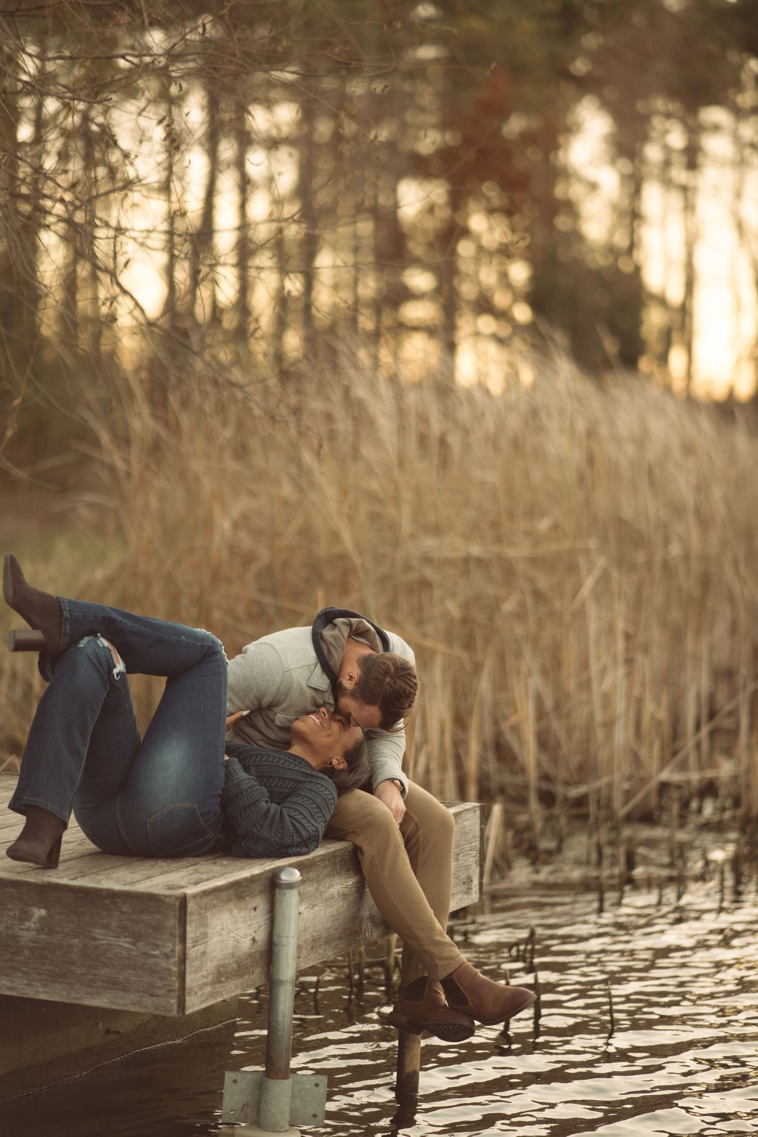 Person lying on a wooden dock at sunset over a tranquil lake surrounded by trees.