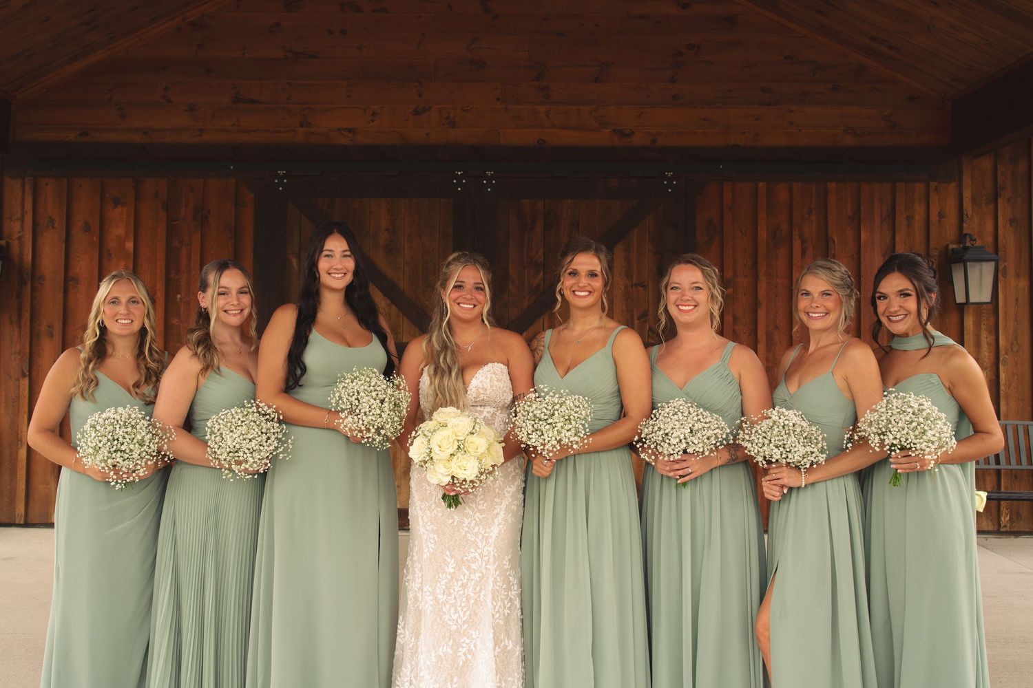 Wedding party in mint green bridesmaid dresses posed in rustic barn setting.