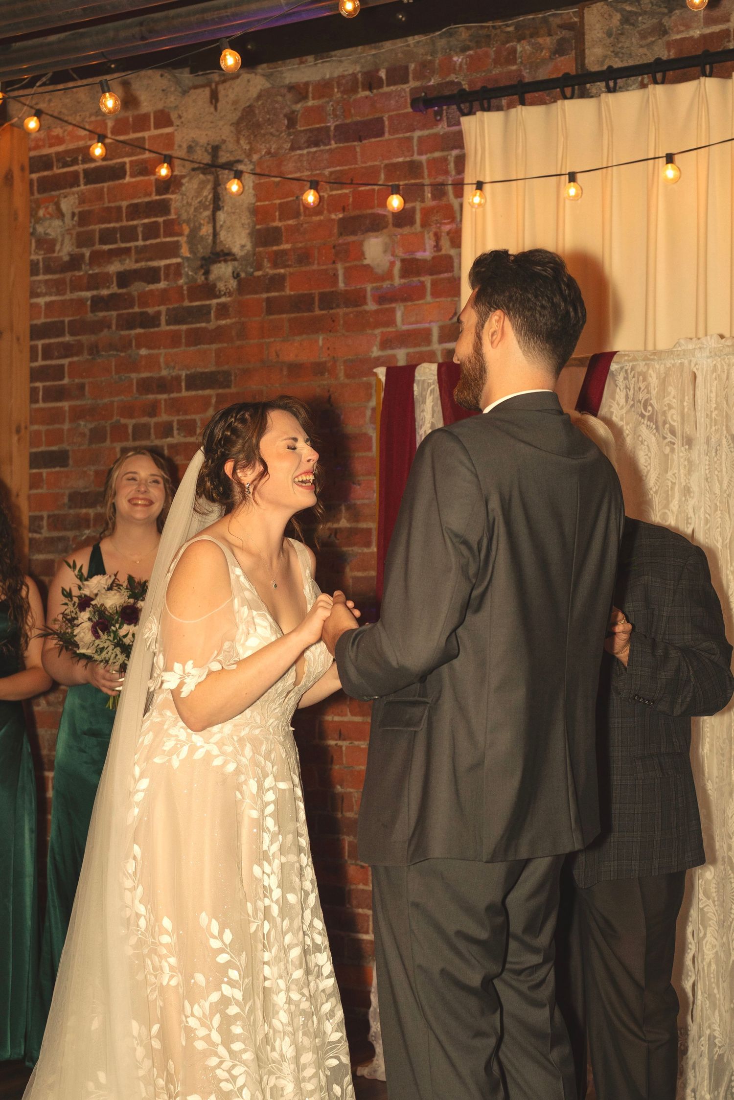Wedding party dancing in line against exposed brick wall with string lights.