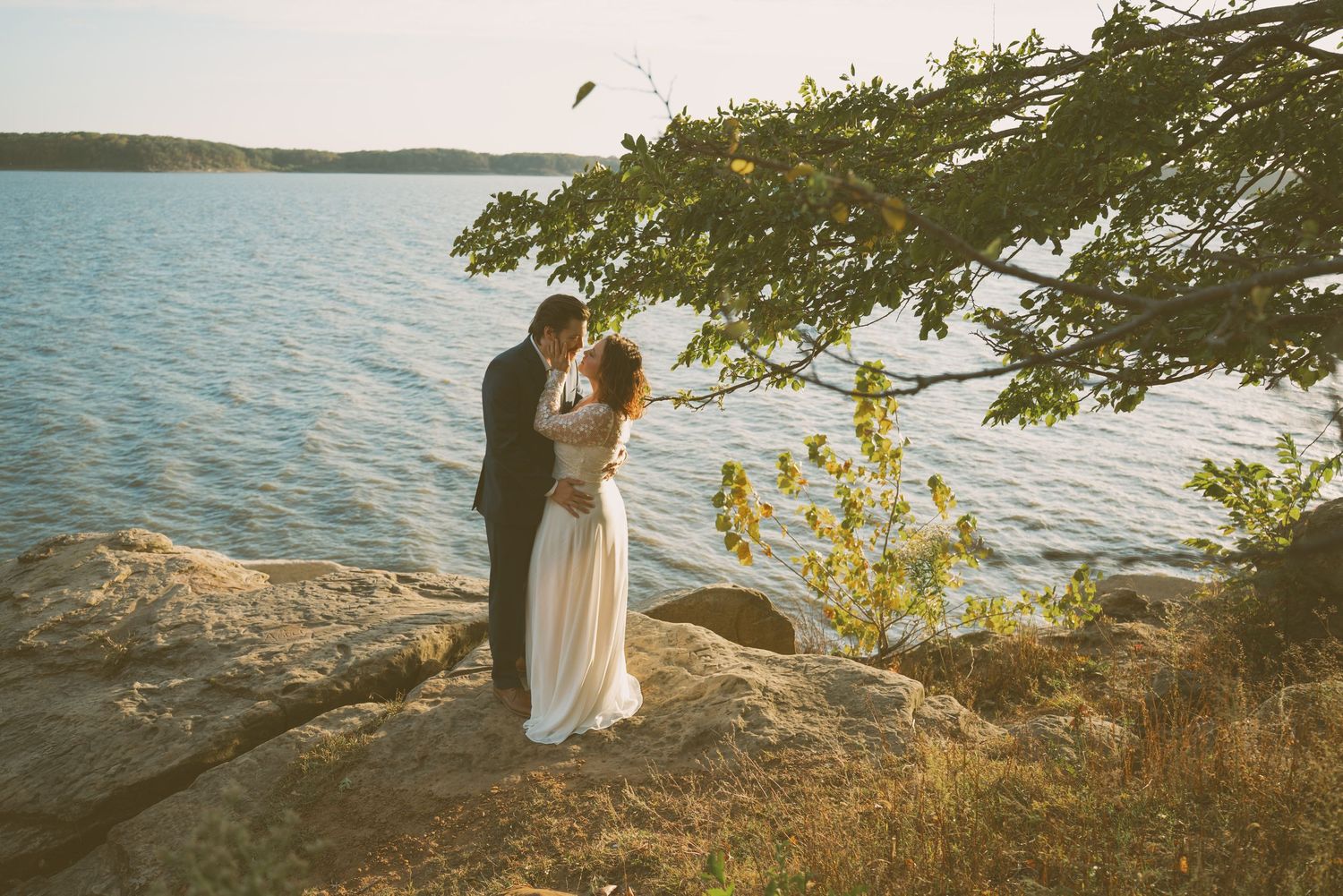 Scenic waterfront engagement photos with couple silhouetted against sunset over the lake.
