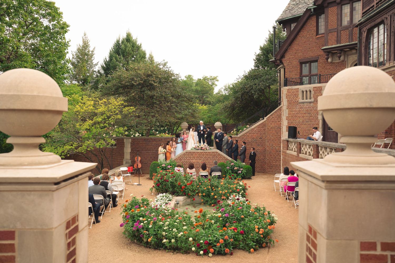 Brick pathway with ornate stone pillars leads through a landscaped garden setting.