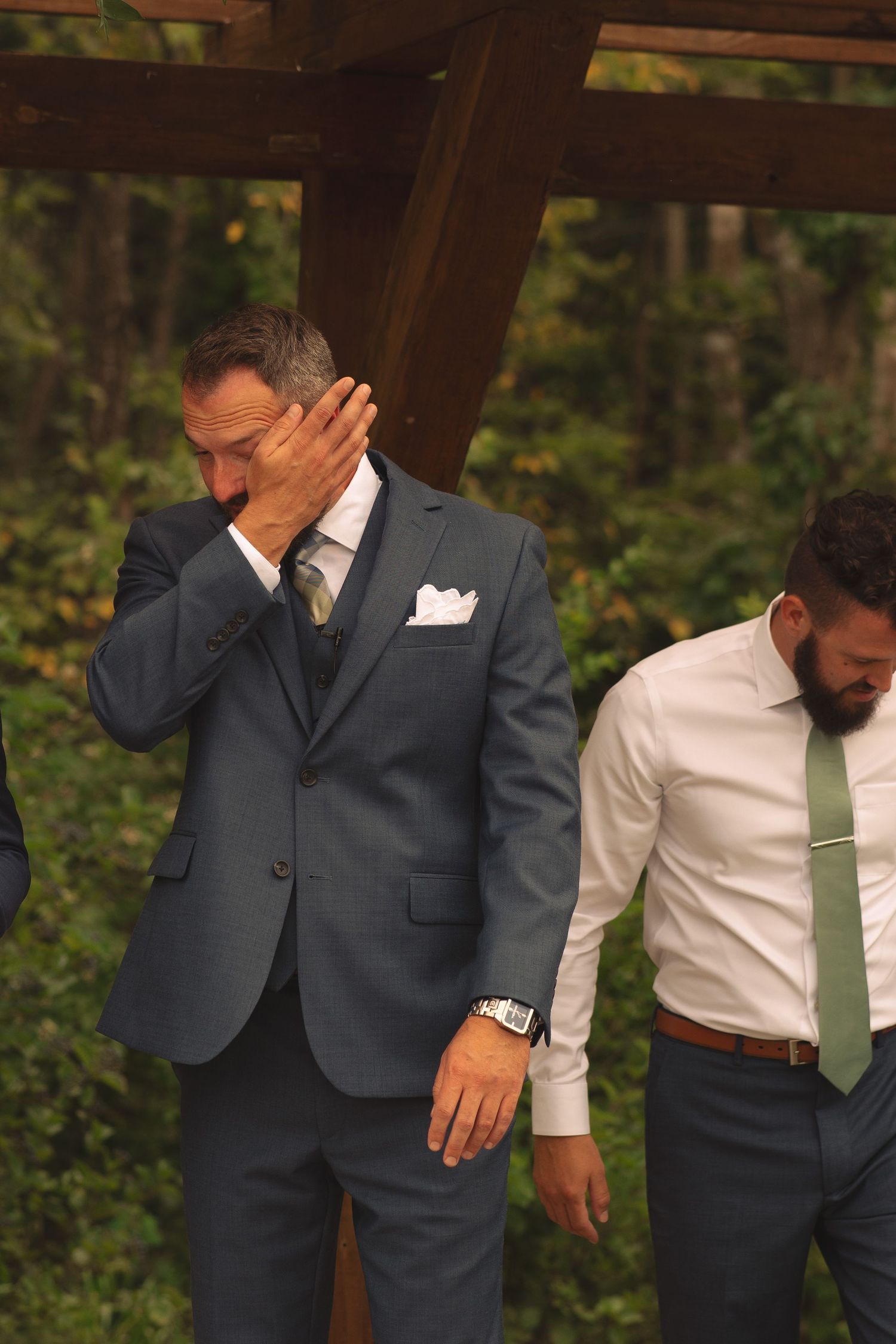 Groomsmen in dark suits show emotional reactions during wedding ceremony.