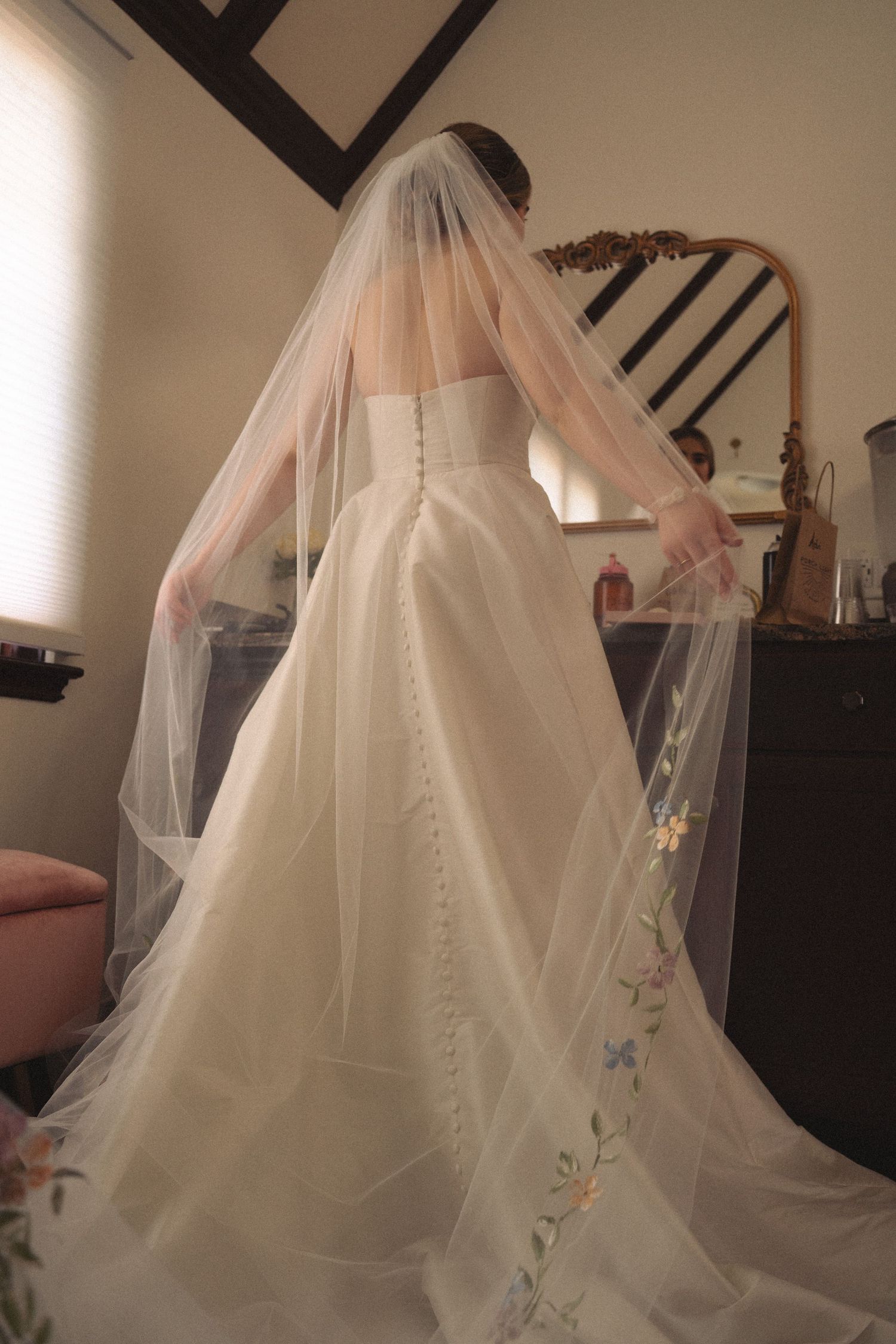 Elegant white wedding veil with delicate embroidered details flowing against a dark interior backdrop.
