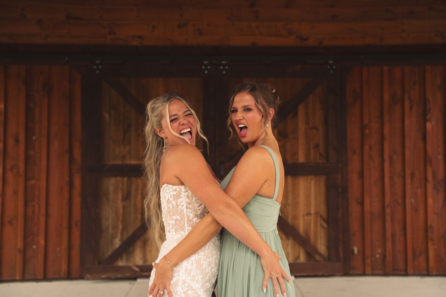 Bridesmaids in sage green dresses pose together at a rustic barn wedding venue.