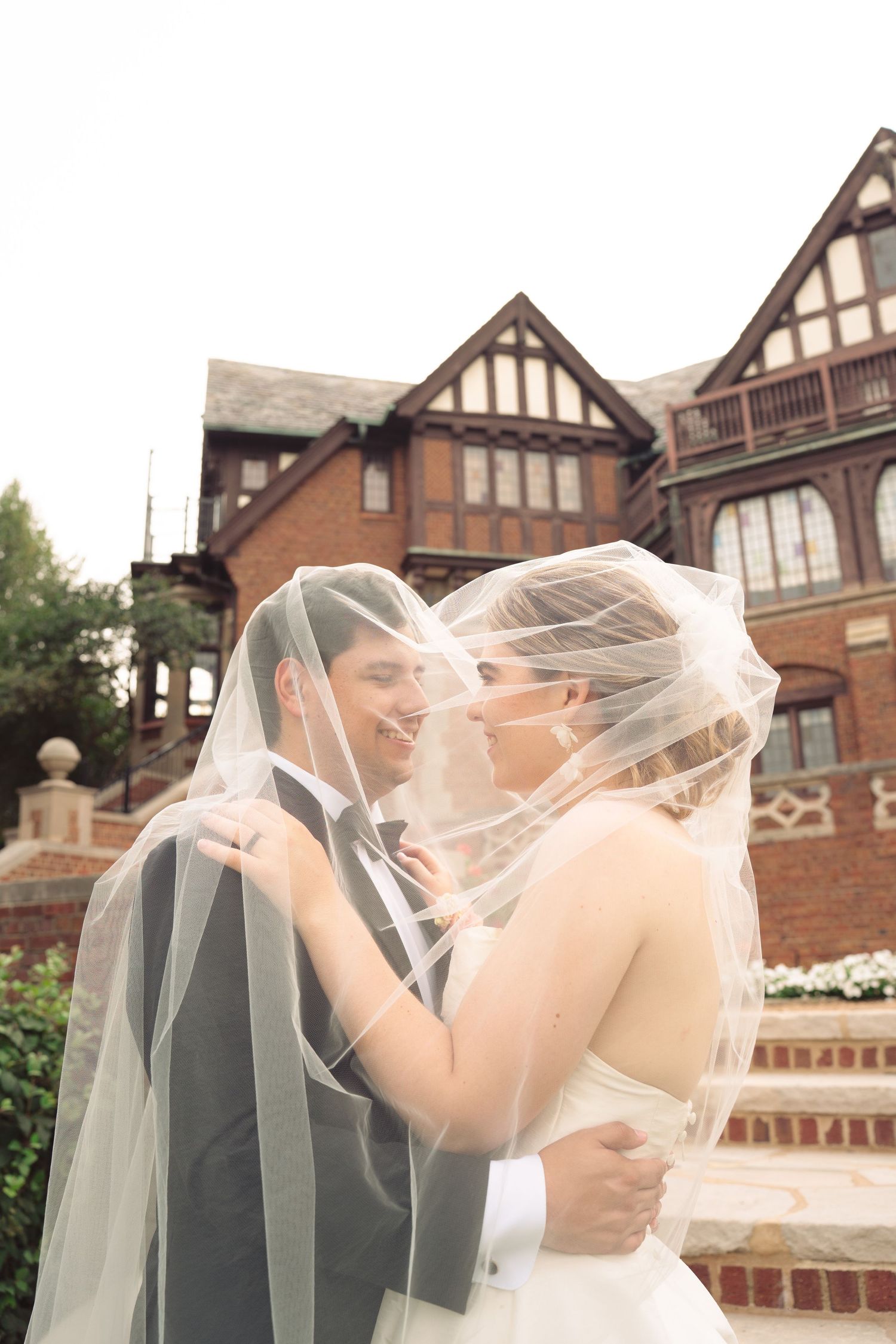 Romantic veiled moment on brick steps of historic mansion.