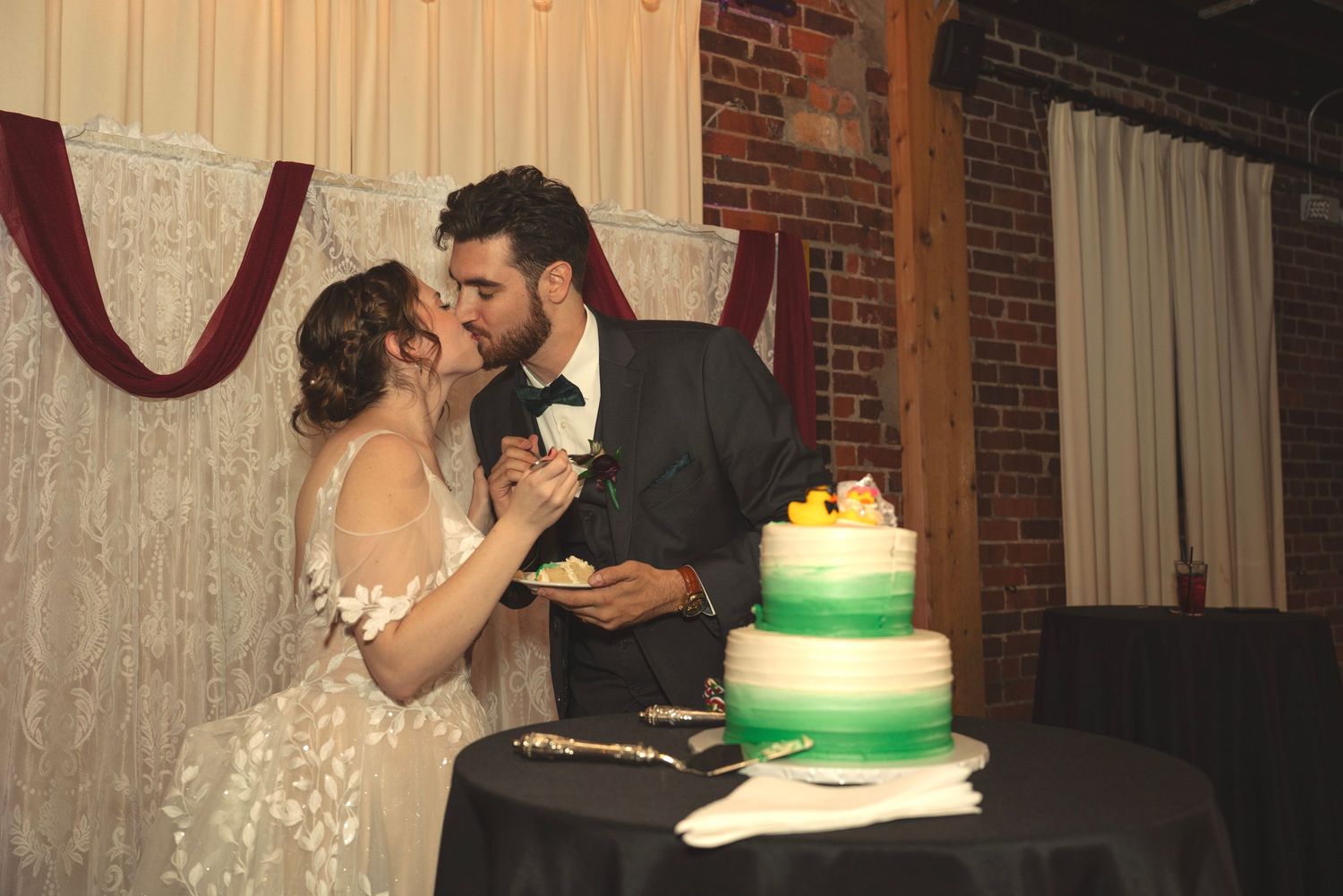 Newlyweds share a playful moment while cutting their green-tiered wedding cake.