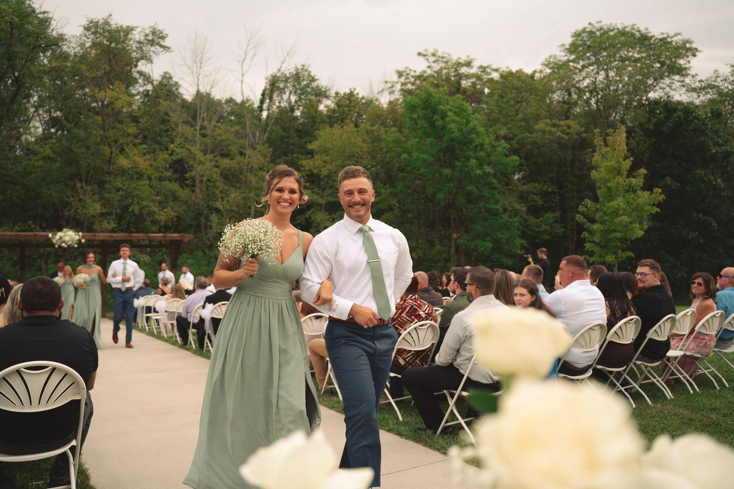 Outdoor wedding ceremony with white chairs and floral decorations in natural setting.