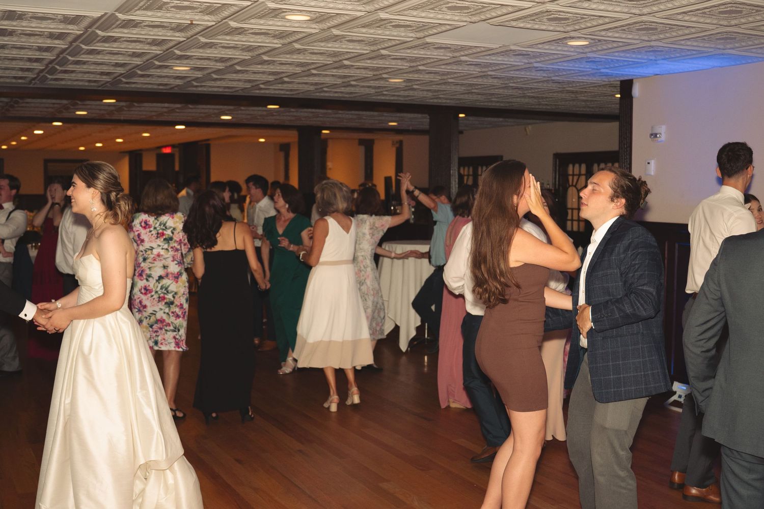 Wedding reception guests dancing in pairs on a polished dance floor with ambient lighting.