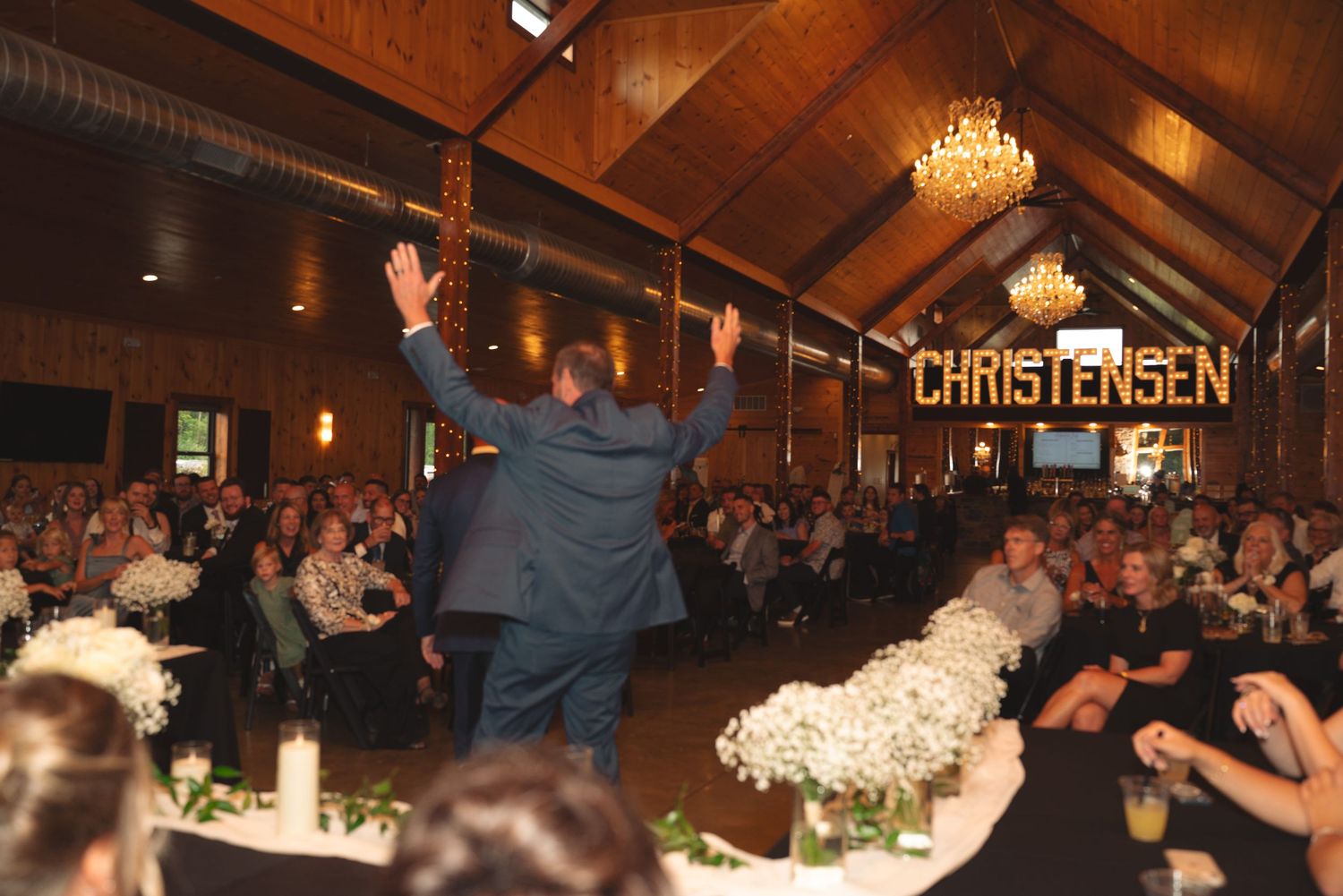 Wedding reception guests dancing under rustic wooden beams and crystal chandeliers at the Christensen venue.