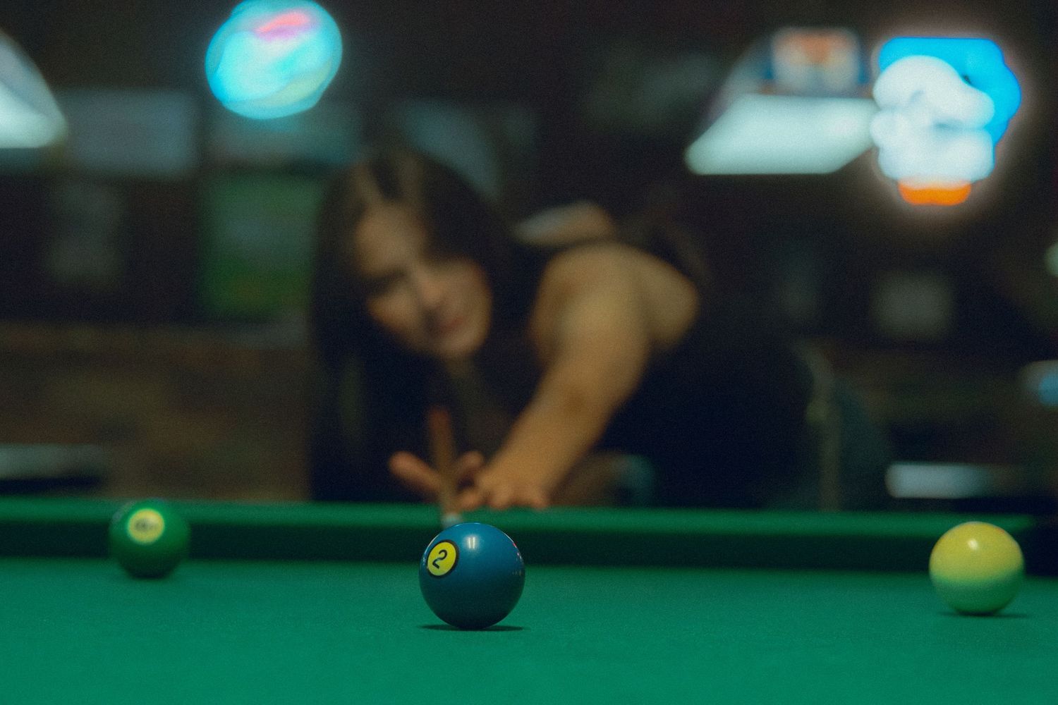 Pool balls and cue sticks on a green felt billiards table in moody lighting.