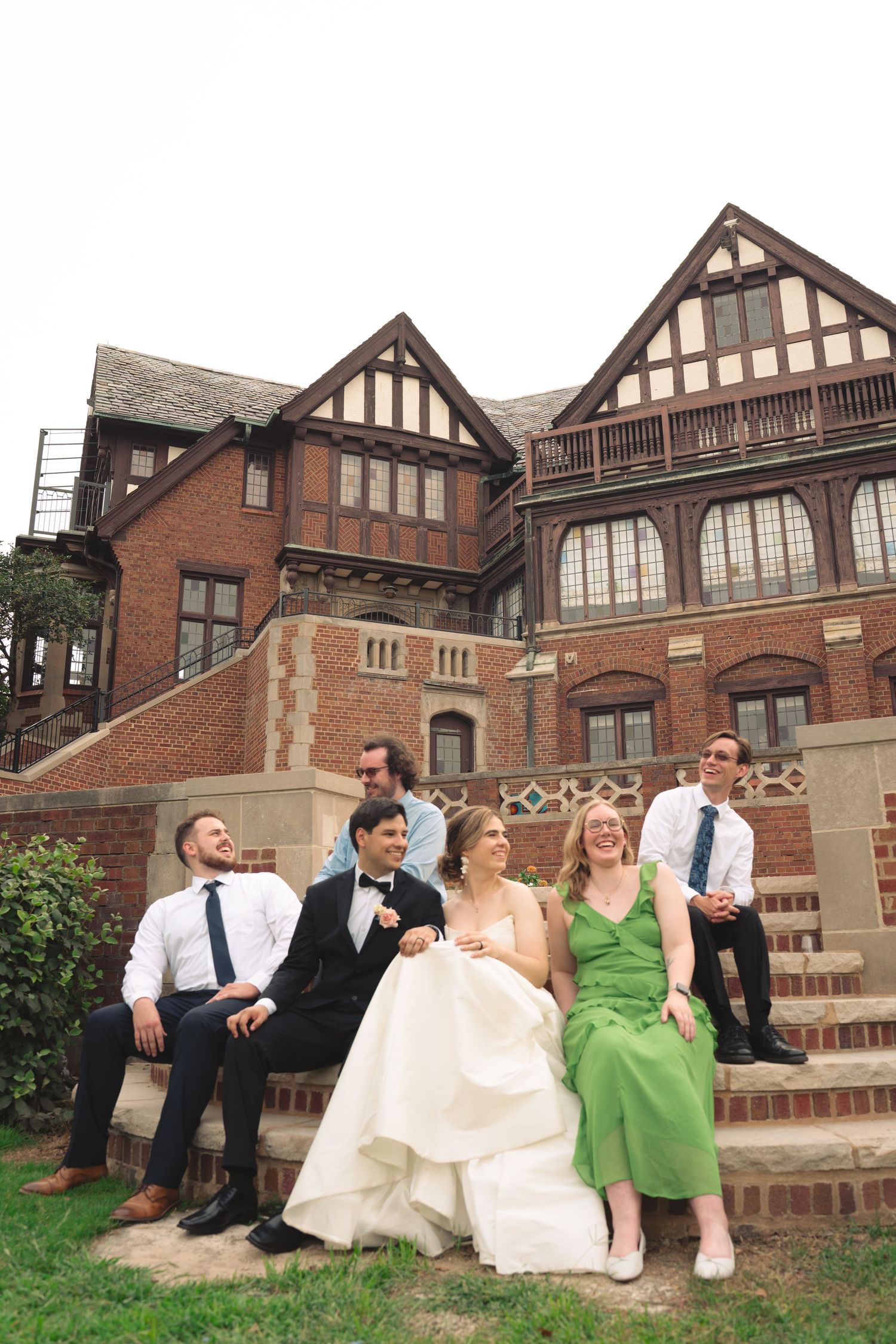 Relaxed wedding group portrait on the steps of a historic brick building.