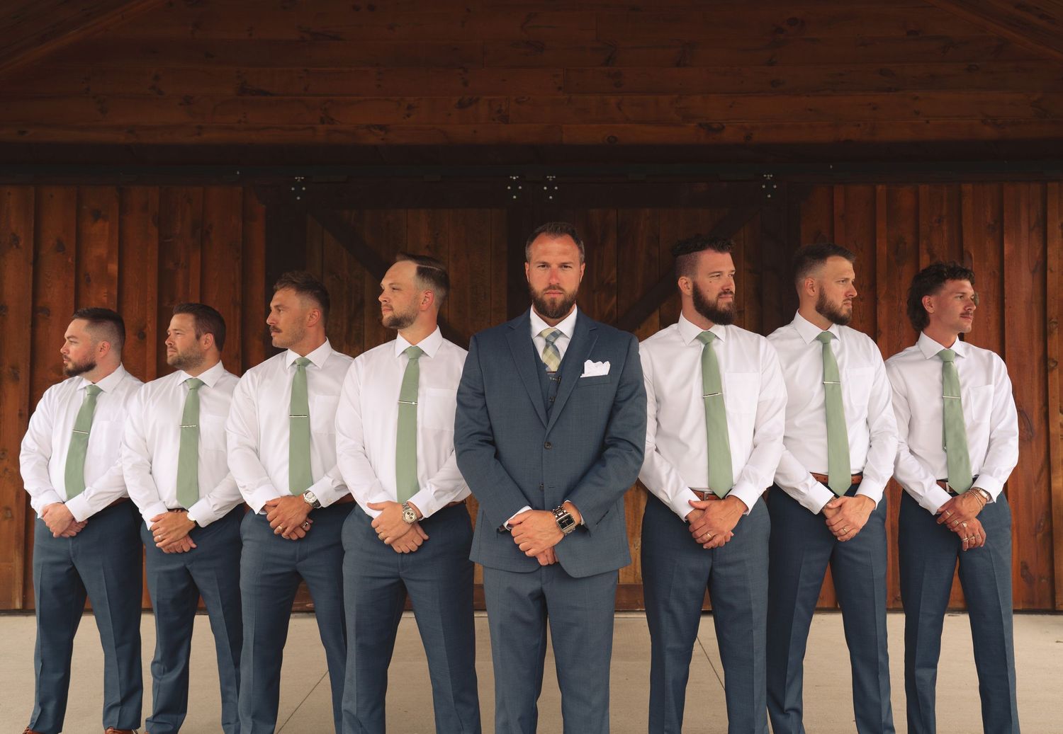 Wedding party members stand in a row showing their matching navy suits and brown leather shoes.