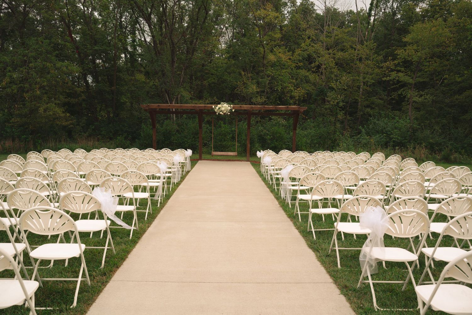Rows of white folding chairs set up for outdoor wedding ceremony with wooded backdrop.