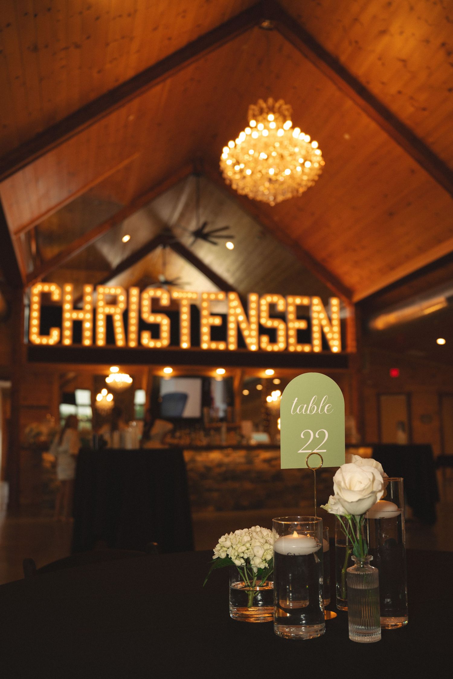 Wedding reception venue with illuminated Christensen sign and table numbers in romantic lighting.