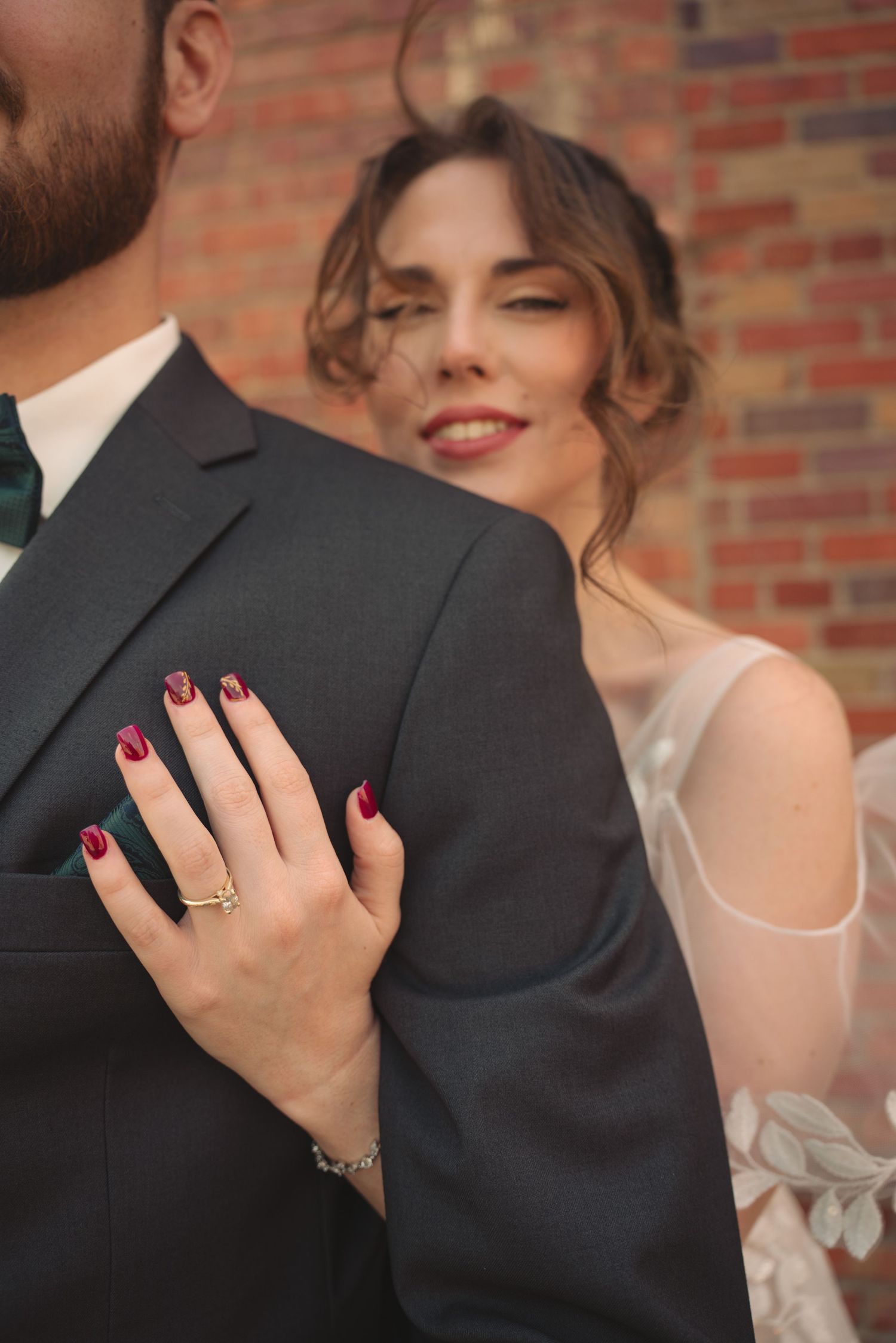 Close-up shot showing red nails against a dark suit jacket during a wedding photo session.