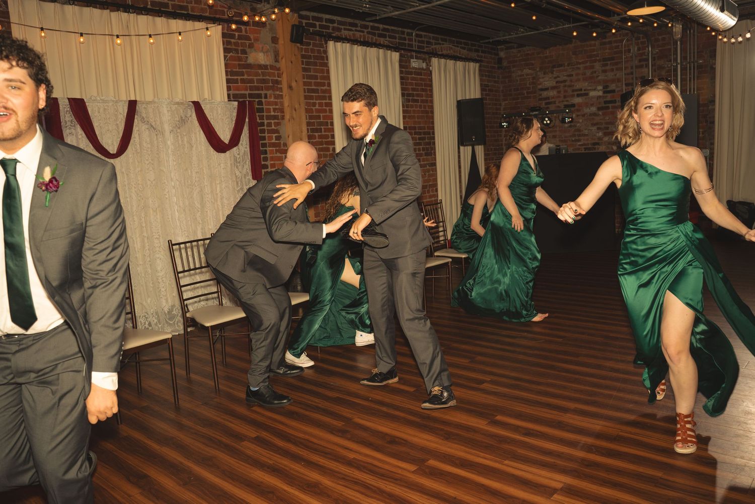 Wedding party members in green dresses and gray suits performing choreographed dance moves.
