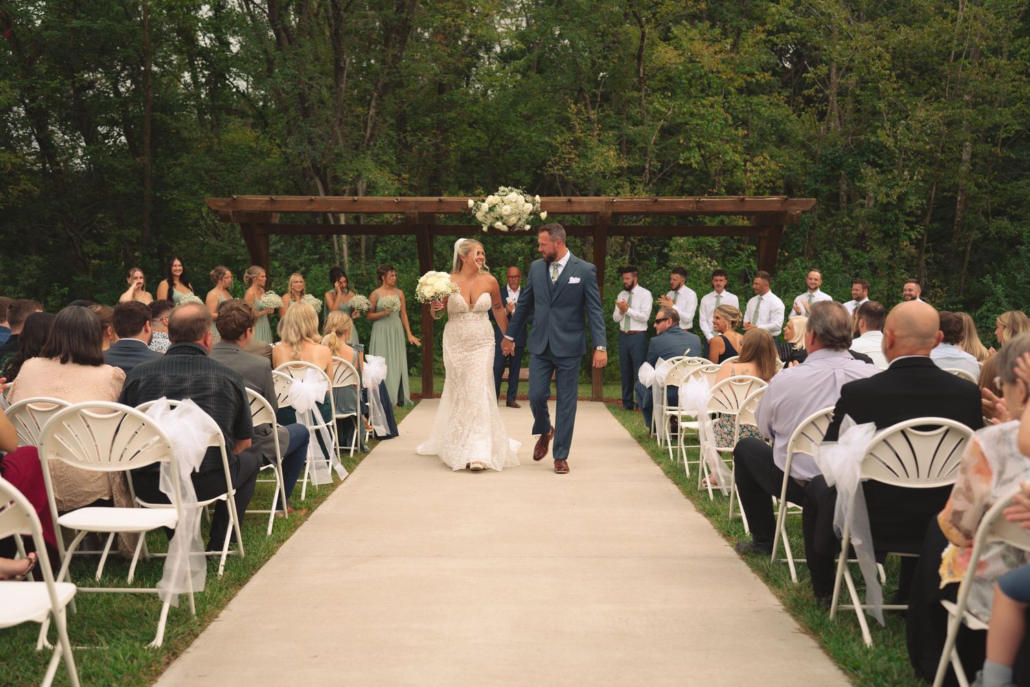 Outdoor wedding ceremony setup with white chairs and floral arch in a garden setting.