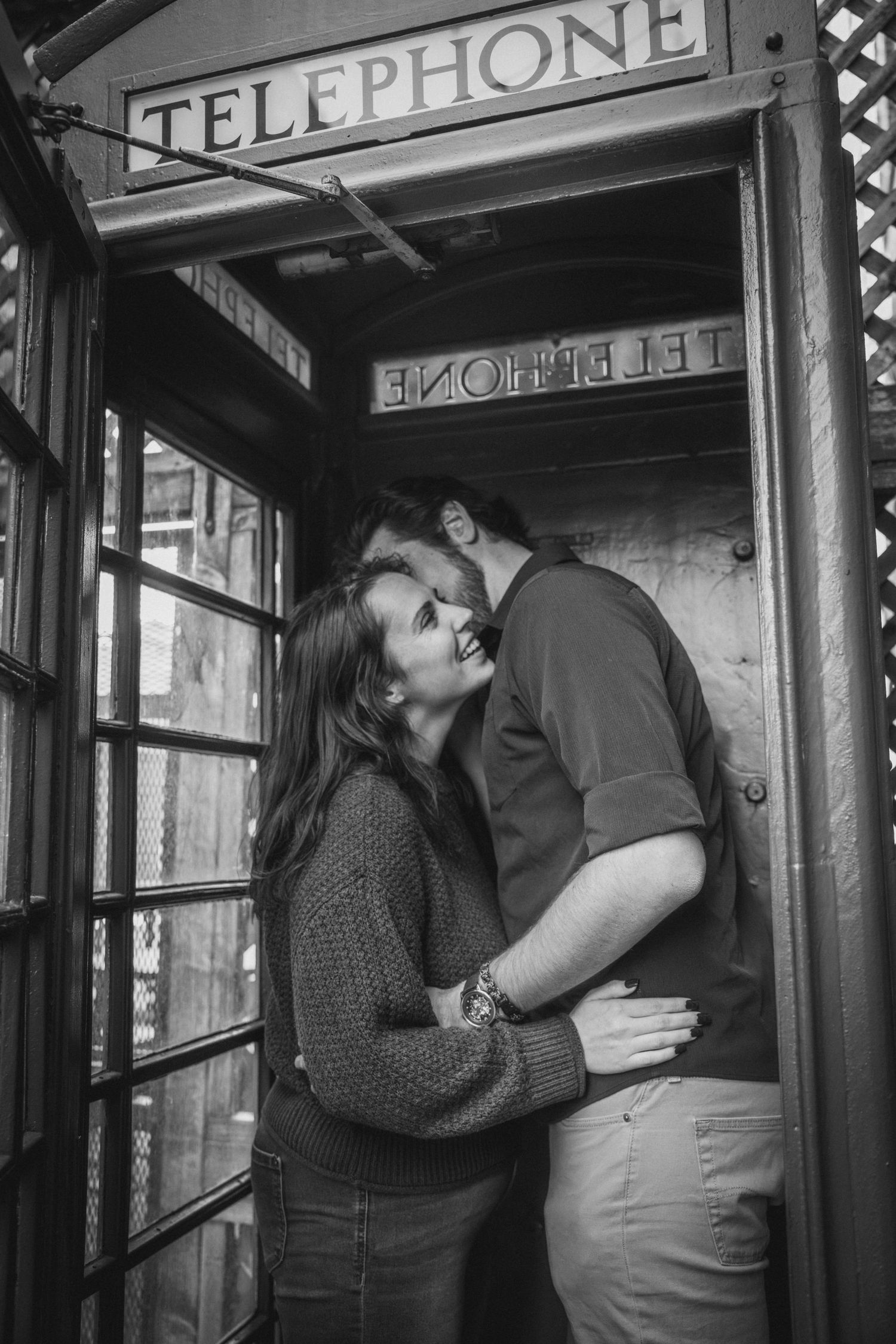 Romantic moment captured in vintage telephone booth with black and white photography.