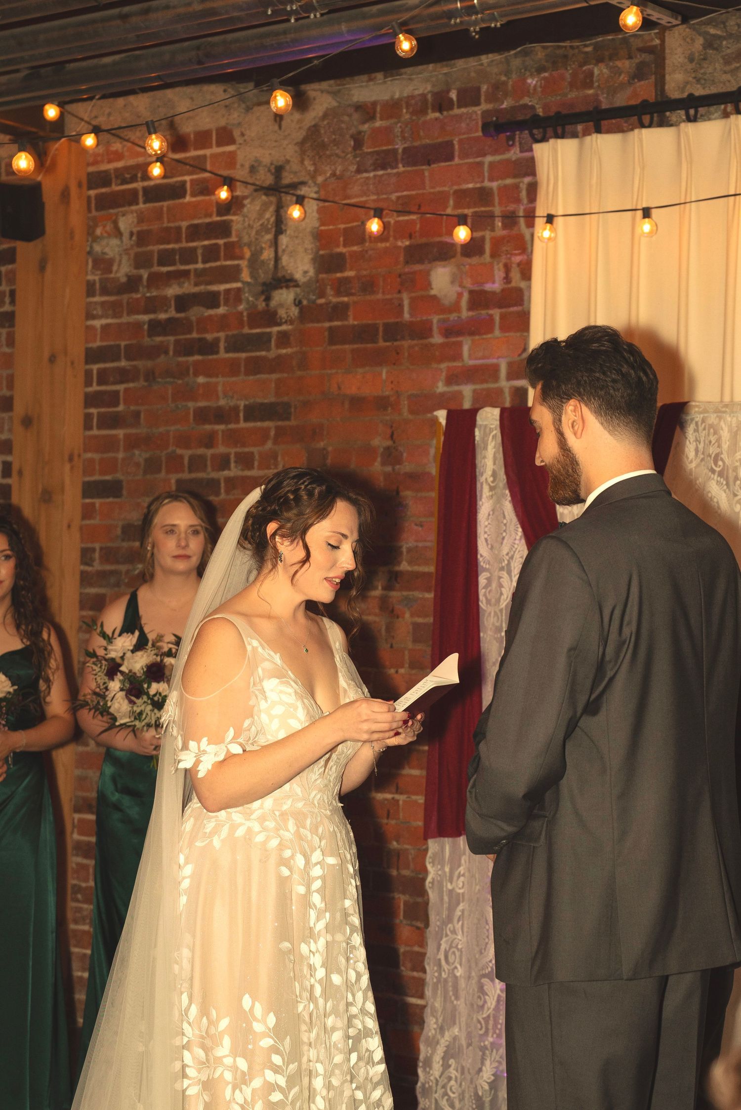 Wedding party and guests mingling in a rustic brick venue decorated with string lights.