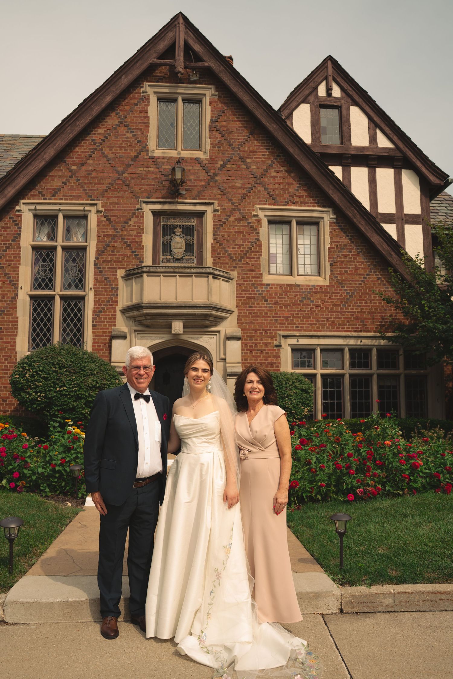 Wedding photos captured outside stately Tudor mansion with red brick facade and blooming garden.