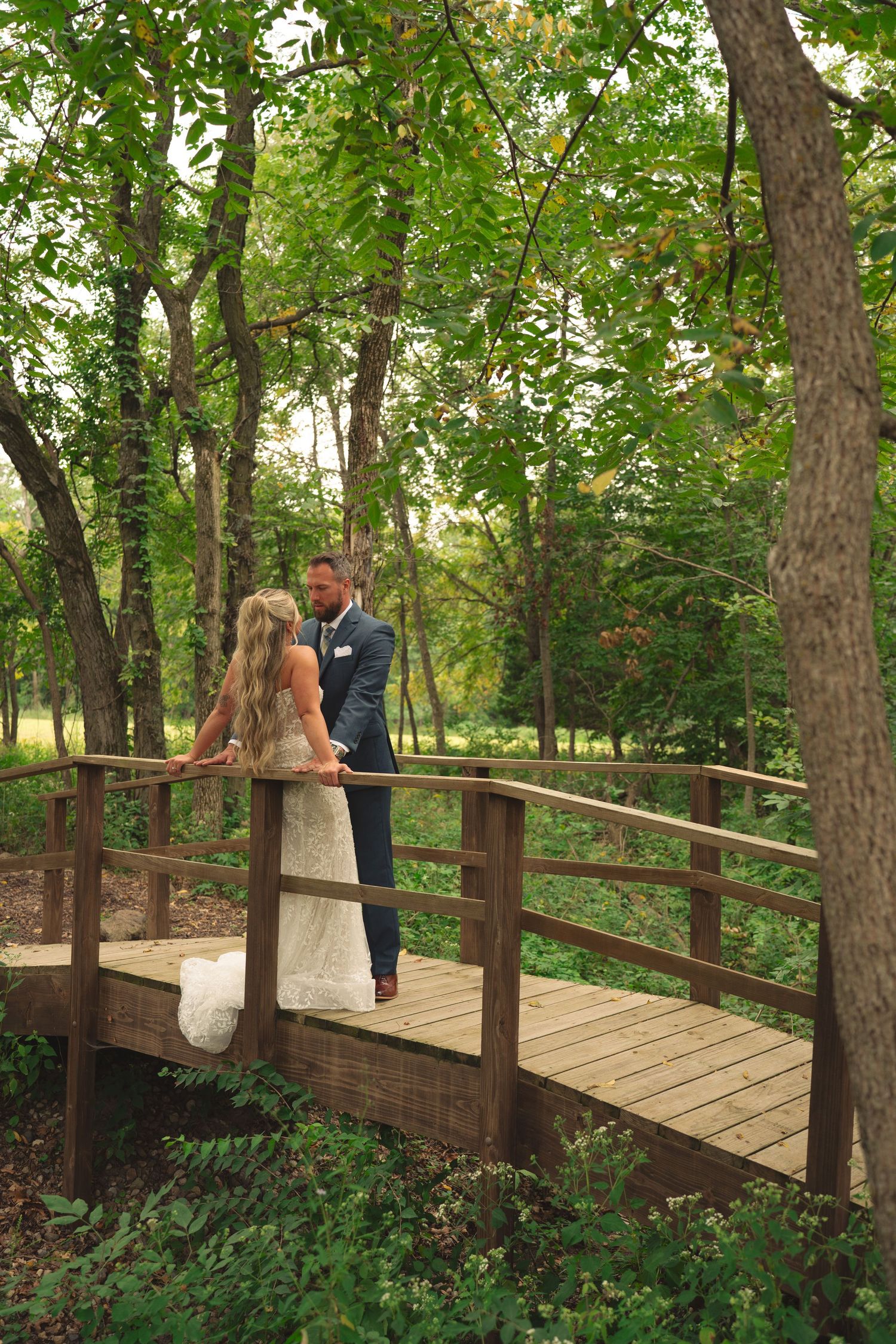 Newlyweds share tender moments on a wooden bridge surrounded by forest greenery.