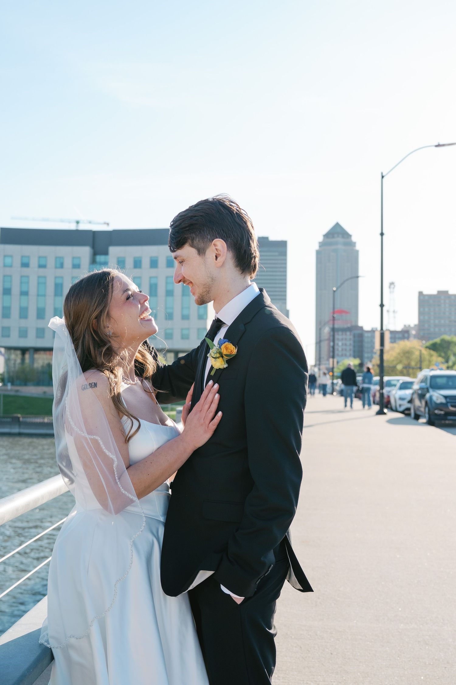 Bride and groom share a romantic moment on a waterfront bridge with a city skyline backdrop on their wedding day.