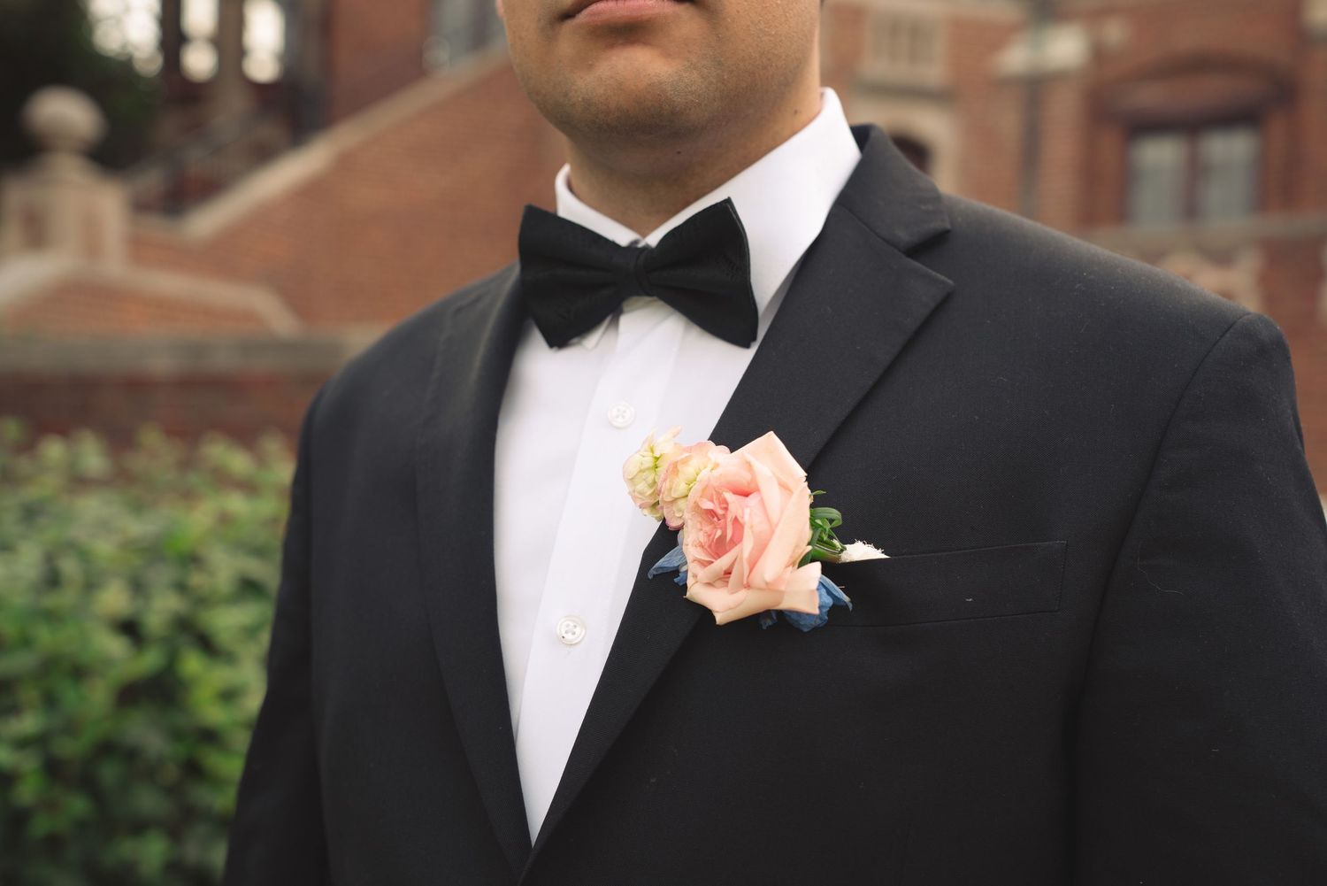 Close-up detail of groom's black bowtie and boutonniere against formal suit.